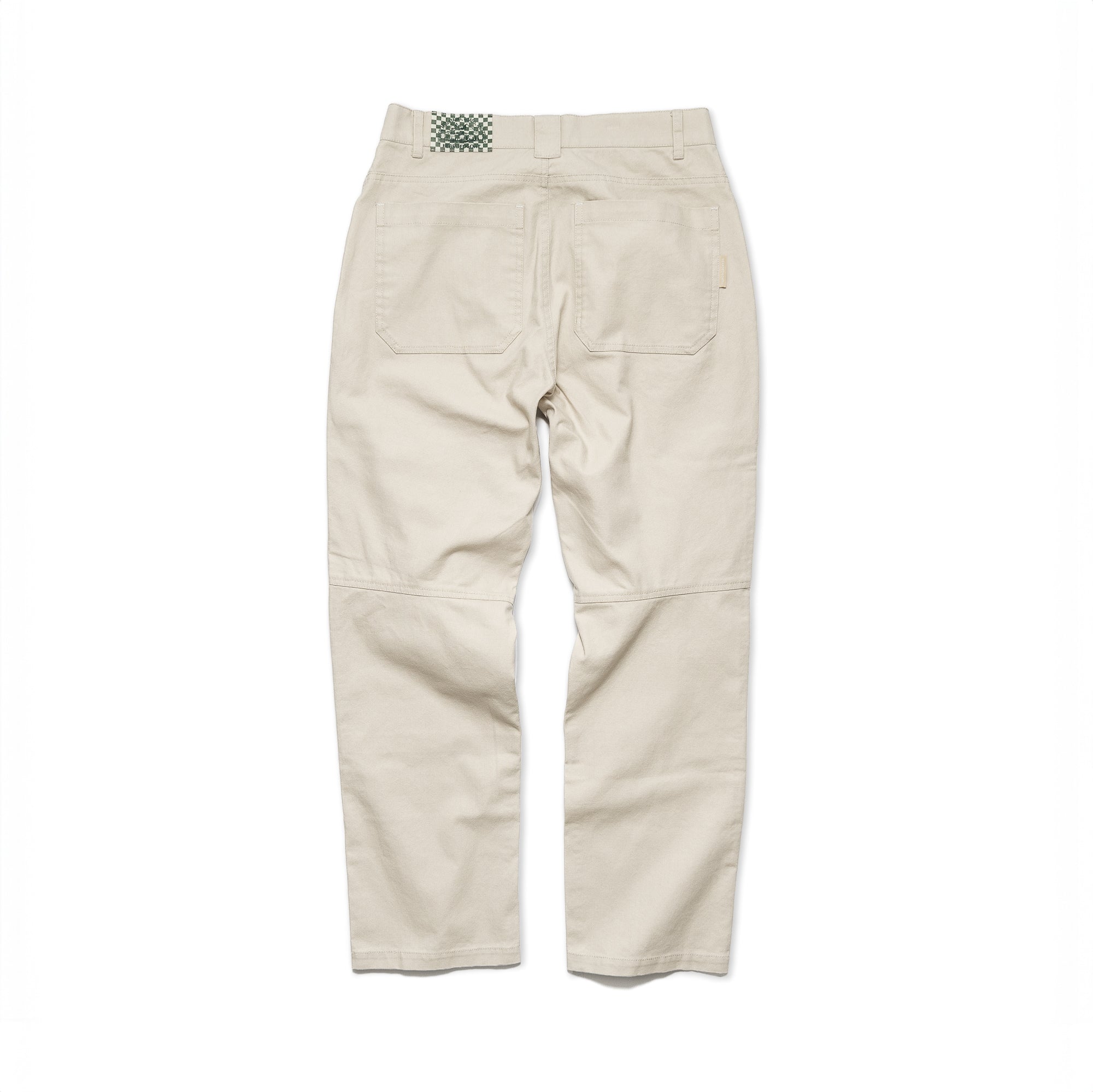 The beardedgoat Mens Foundry Canvas Pant in beige is shown from the back, featuring durable cotton canvas, patch pockets, belt loops, a green-and-white checkered waistband tag, knee seams, and double-layered knees for extra durability.