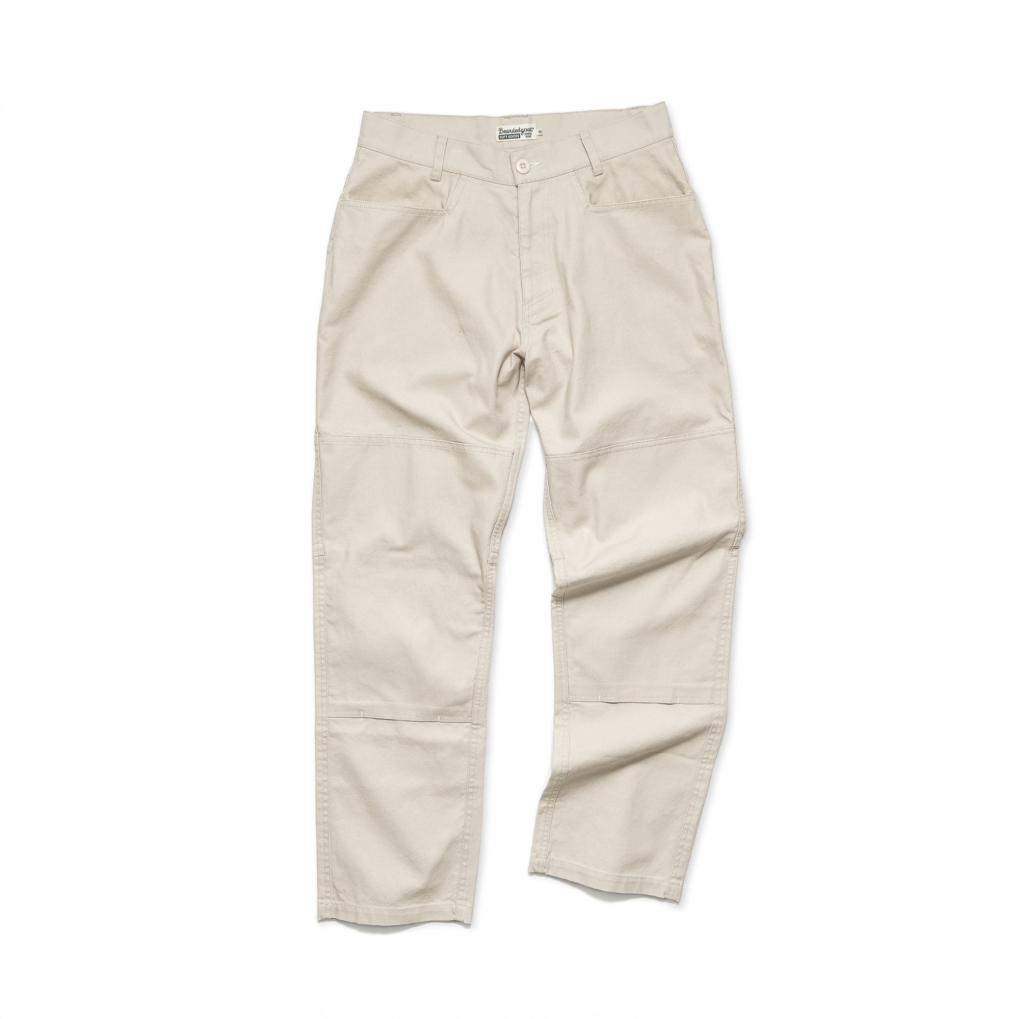 The beardedgoat Mens Foundry Canvas Pant in light beige, made from durable cotton canvas with double-layered knees, reinforced pockets, belt loops, and a button-zip closure, is shown laid flat on a white background.