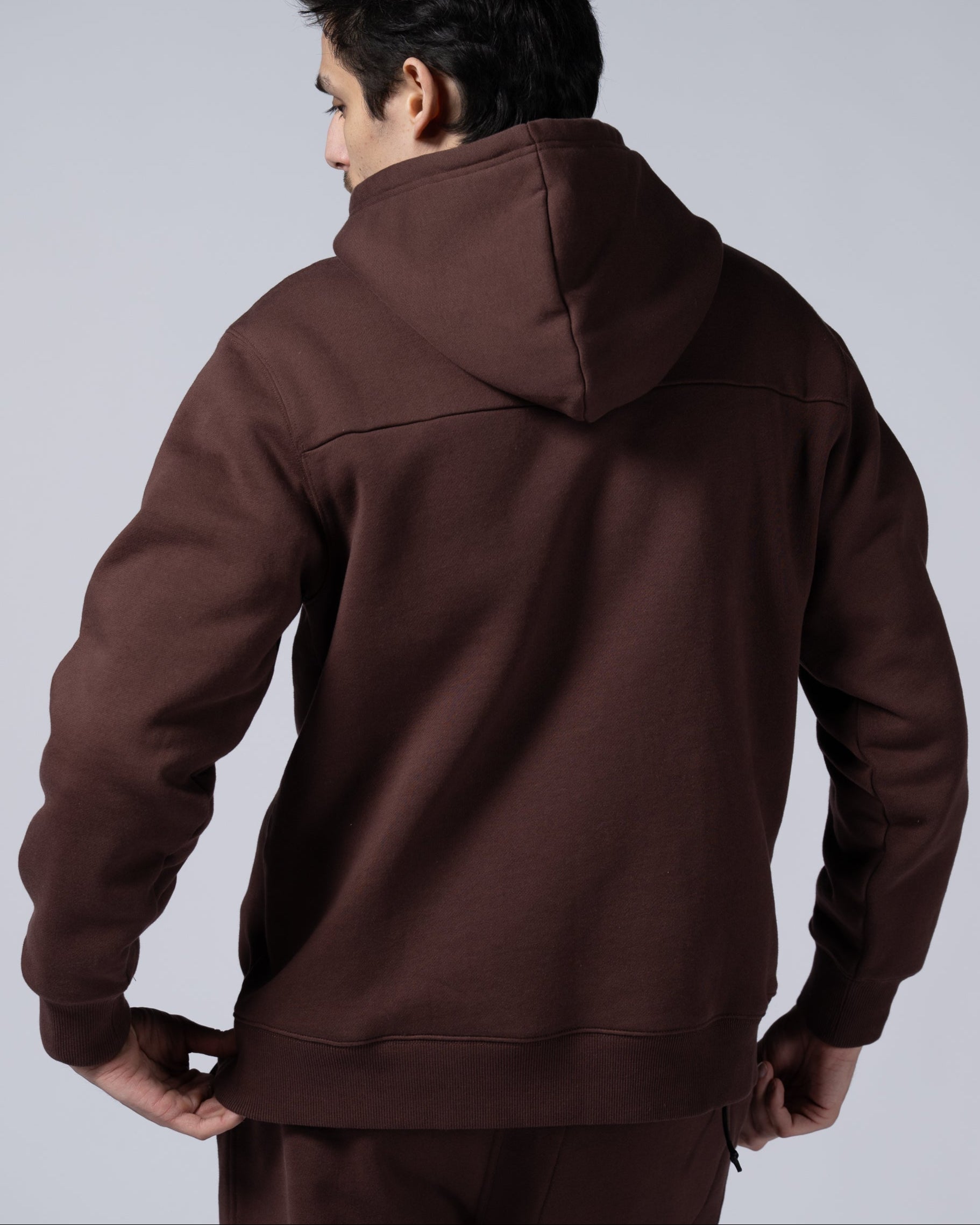 A person with dark hair faces away from the camera, wearing the beardedgoat Mens Void Hoodie, made of heavyweight cotton fleece, ideal for post-ride recovery, against a plain light background.