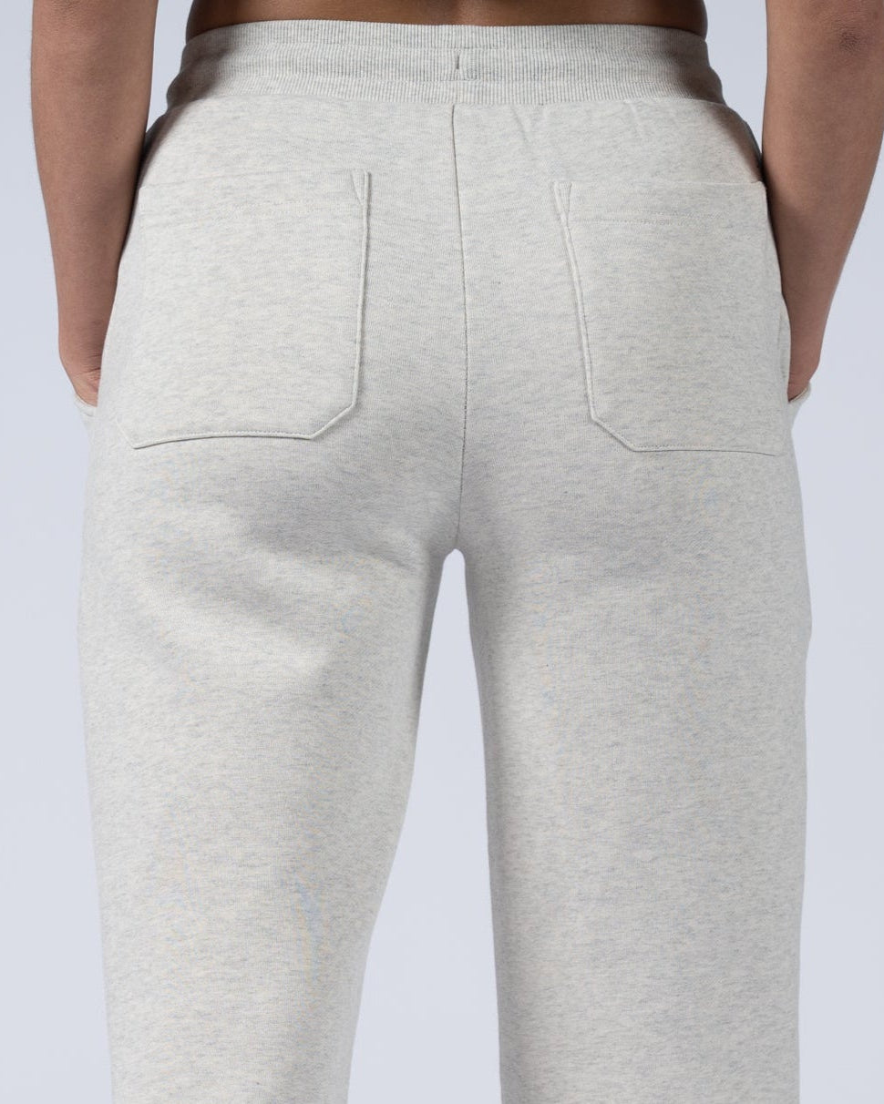 A person faces away from the camera, wearing beardedgoat’s Women’s Overnight Sweatpant in light gray heavyweight cotton fleece with two back pockets and a relaxed fit, paired with white sneakers. The background is plain and light.