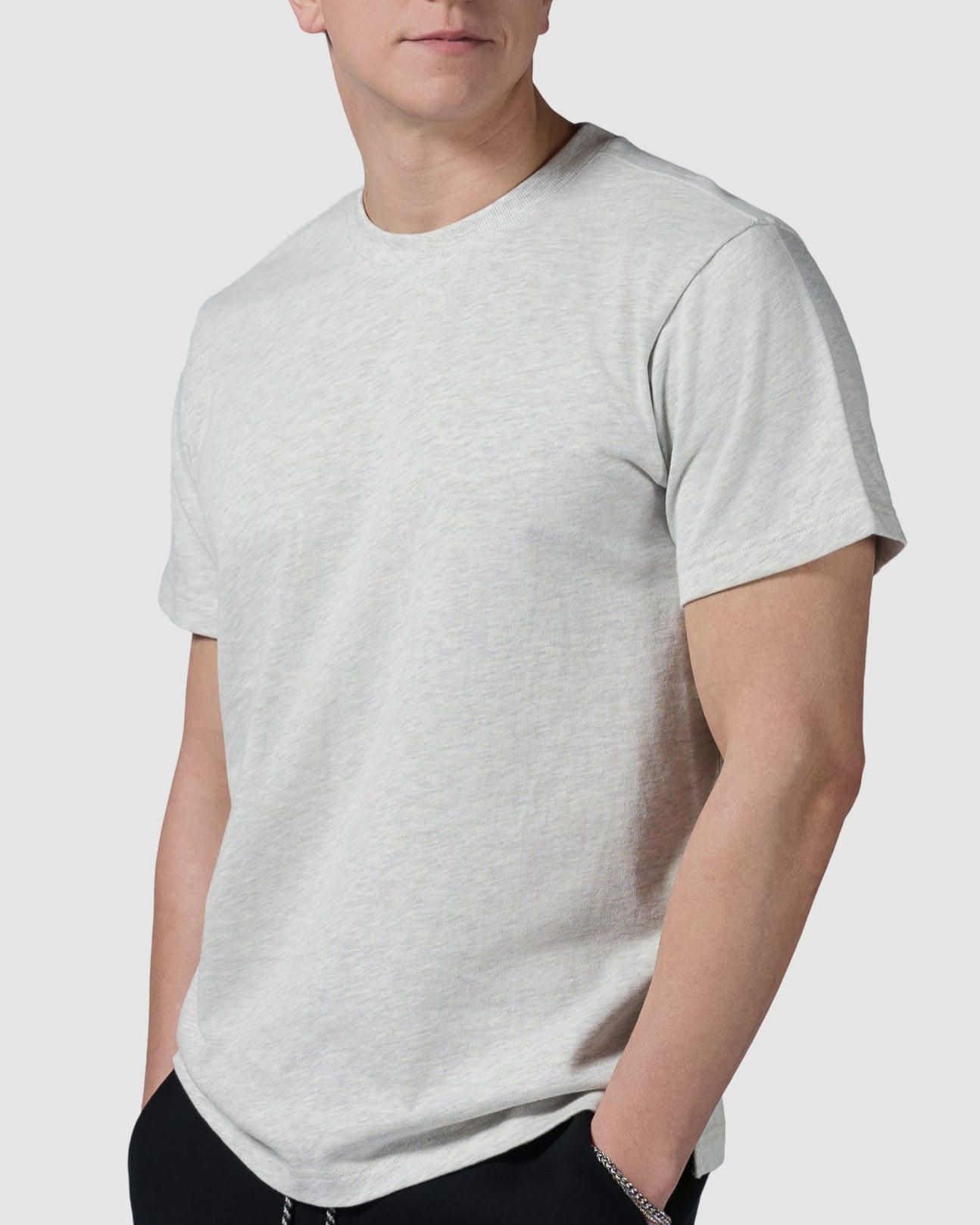 A young man wearing the BEARDEDGOAT Mens Valley Tee in light gray and black pants with white drawstrings stands with his hands in his pockets, looking slightly to the side against a plain light background.