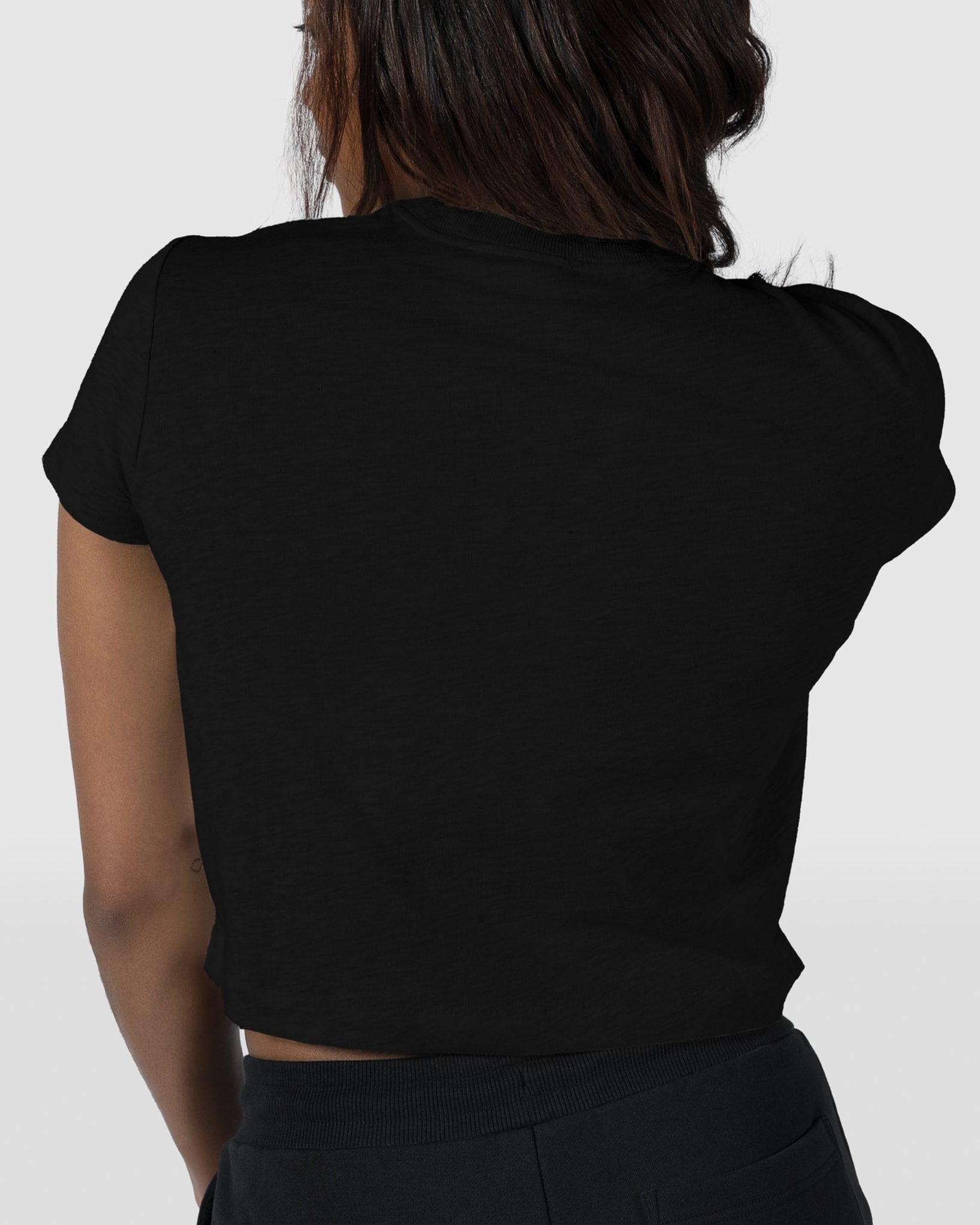 A woman with medium-length dark hair is shown from the back wearing the BEARDEDGOAT Womens Valley Tee in black, standing against a plain light gray background—an ideal look for easy summer days.