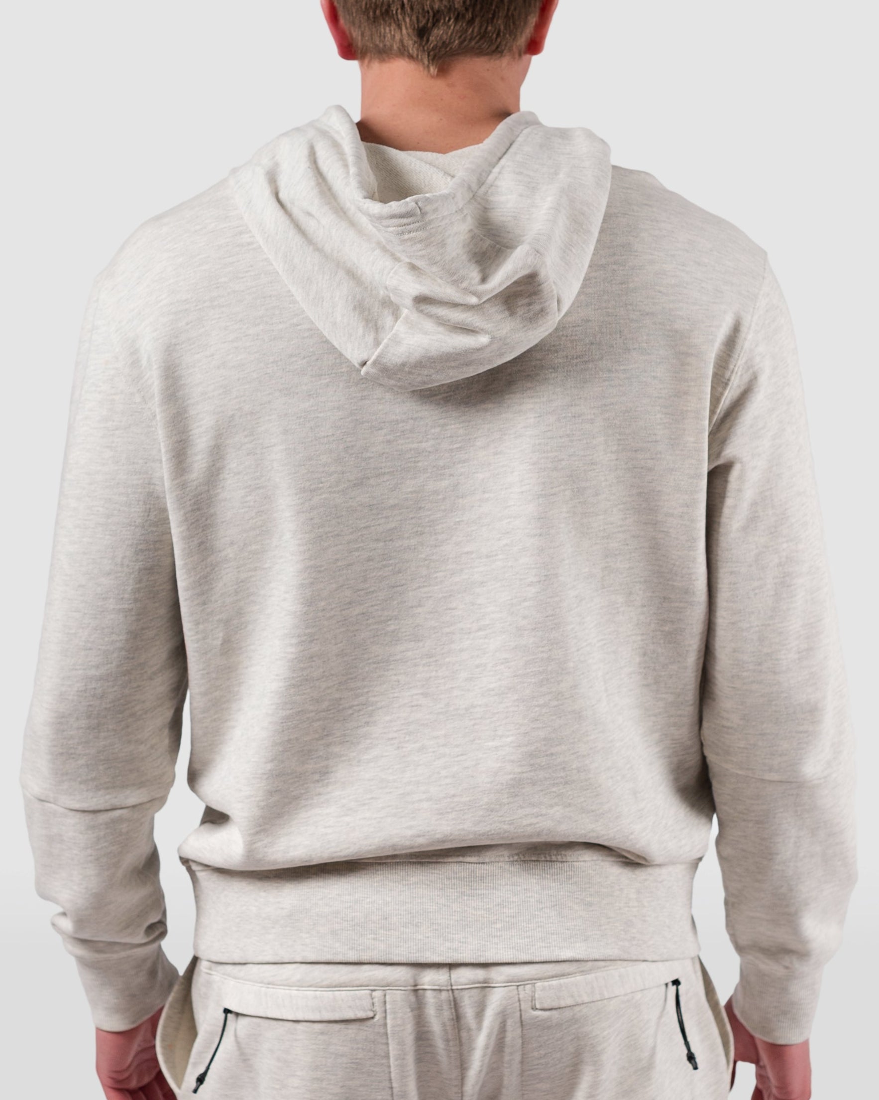 A person wearing the BEARDEDGOAT Mens Drift Hoodie and matching sweatpants in light gray stands facing away, showcasing the back of the outfit against a plain light background—ideal for spring to summer wear.