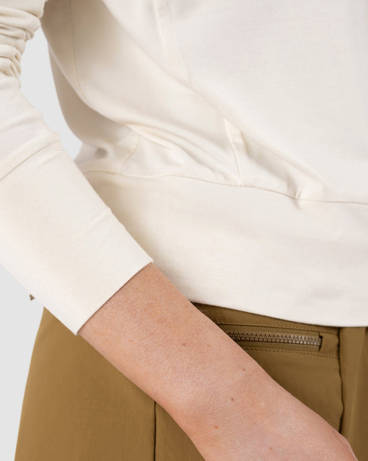 A woman models the BEARDEDGOAT Womens EverZen Hoodie, a long-sleeve off-white top made from hypoallergenic bamboo fibers, shown from the side against a plain background.