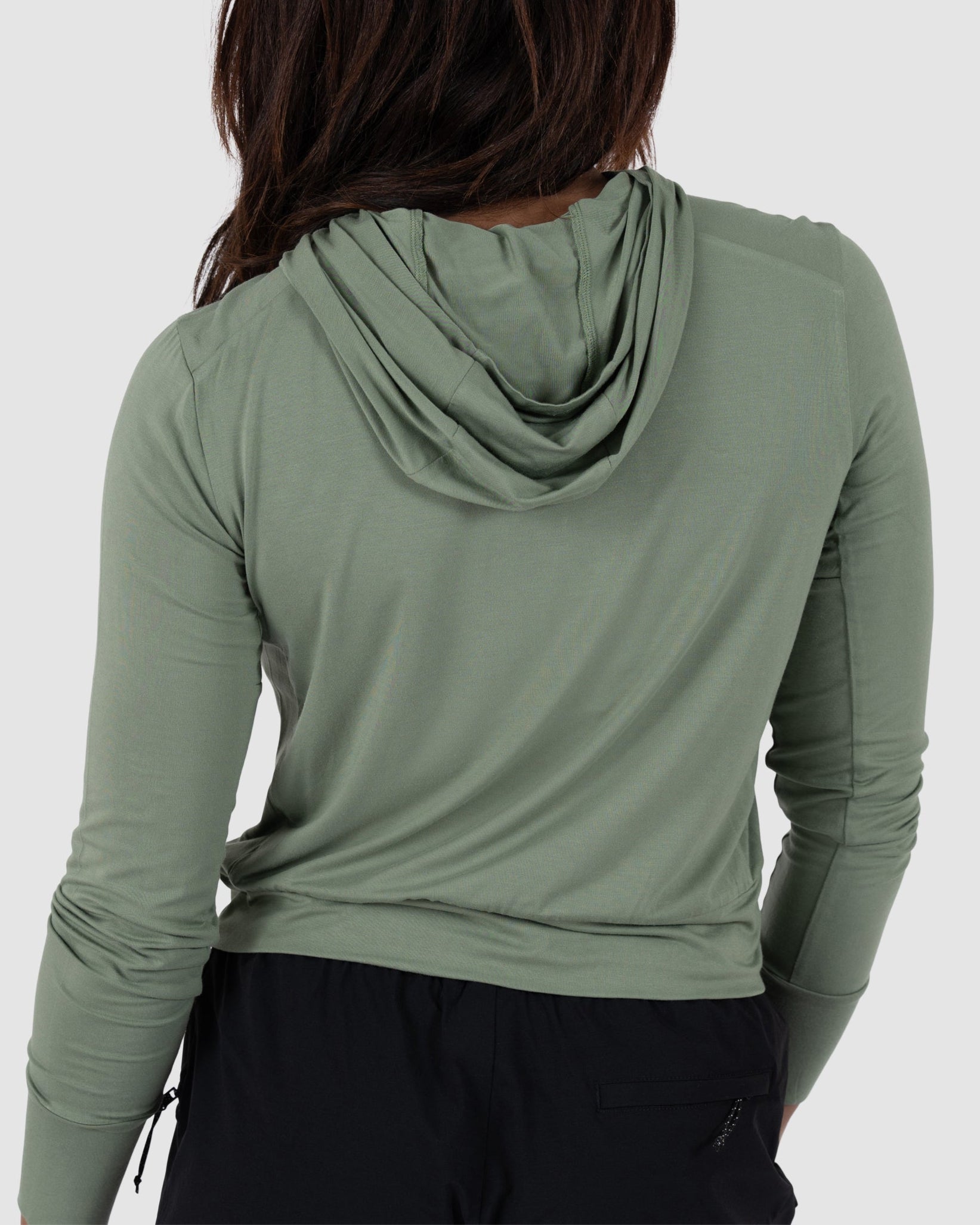 A person with long brown hair is seen from behind, wearing the BEARDEDGOAT Womens EverZen Hoodie in light green bamboo fabric and black pants against a plain light background.