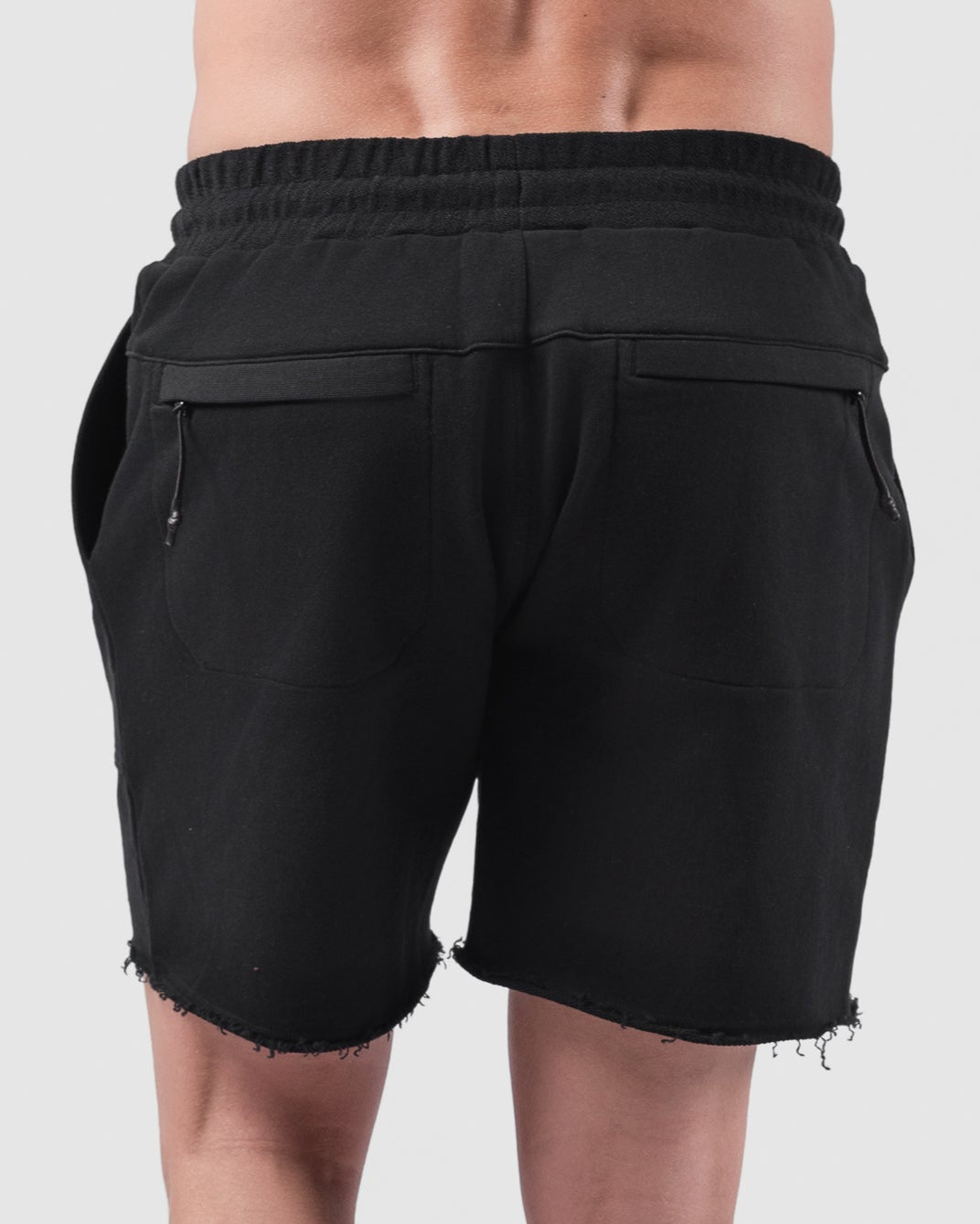 A person faces away from the camera in BEARDEDGOAT Mens Drift Short, crafted from lightweight terry, featuring frayed hems and back pockets. Theyre styled with white crew socks and sneakers against a plain, light backdrop.