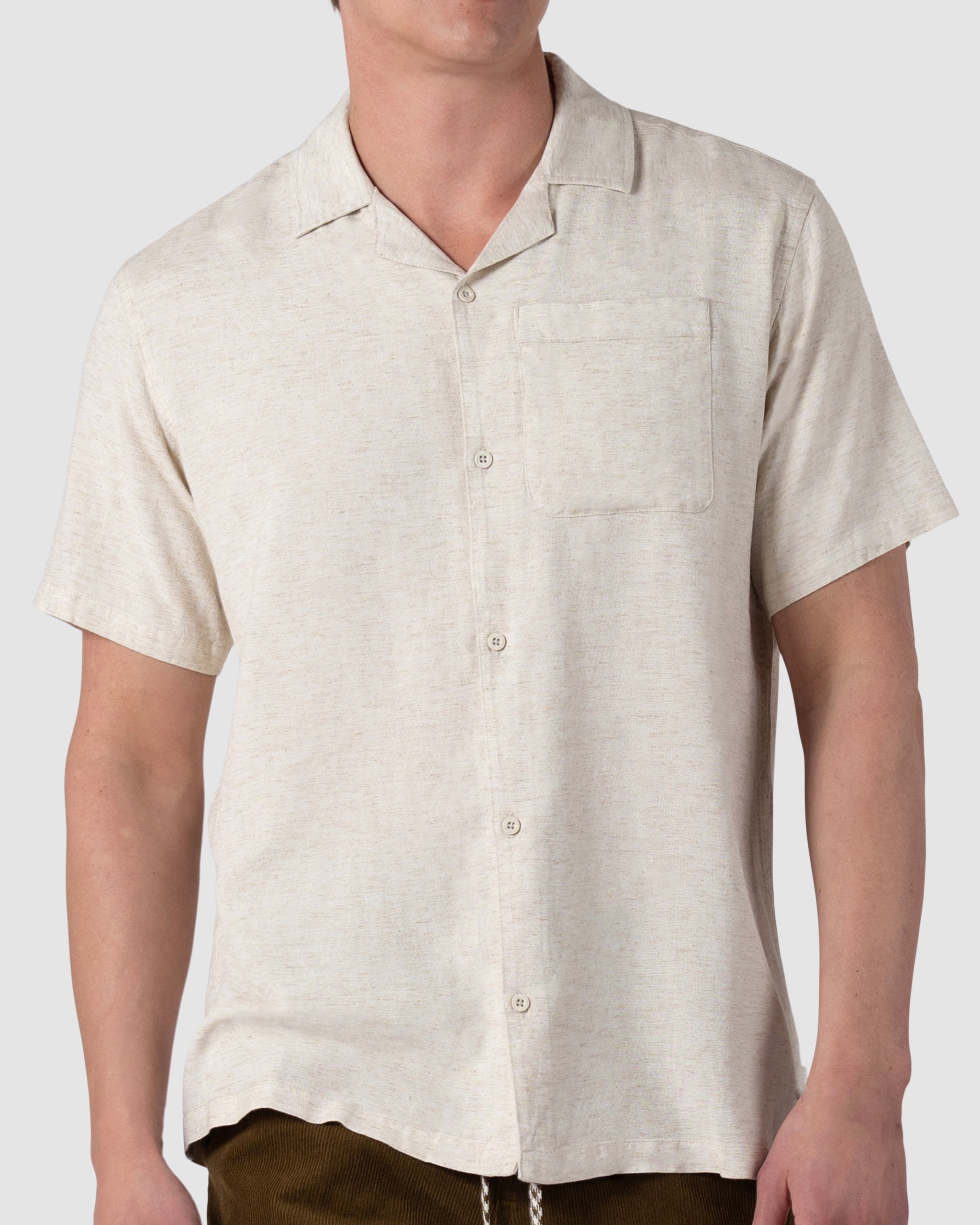 A man models the BEARDEDGOAT Mens Breeze Shirt, a lightweight linen short-sleeve button-up with collar and chest pocket, standing against a plain light gray background.