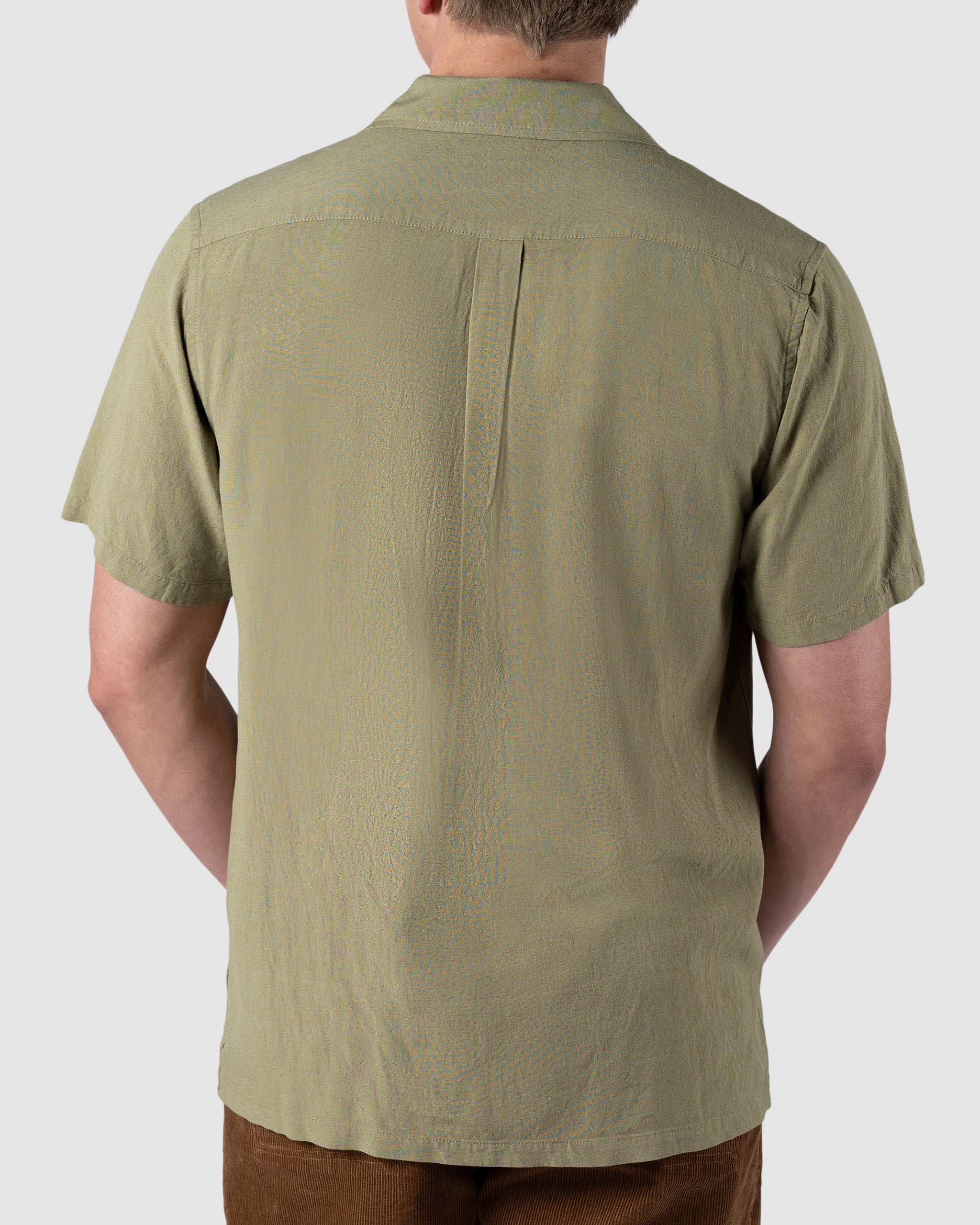 A person is seen from the back wearing the BEARDEDGOAT Mens Breeze Shirt in light olive green with brown pants, set against a plain light background.