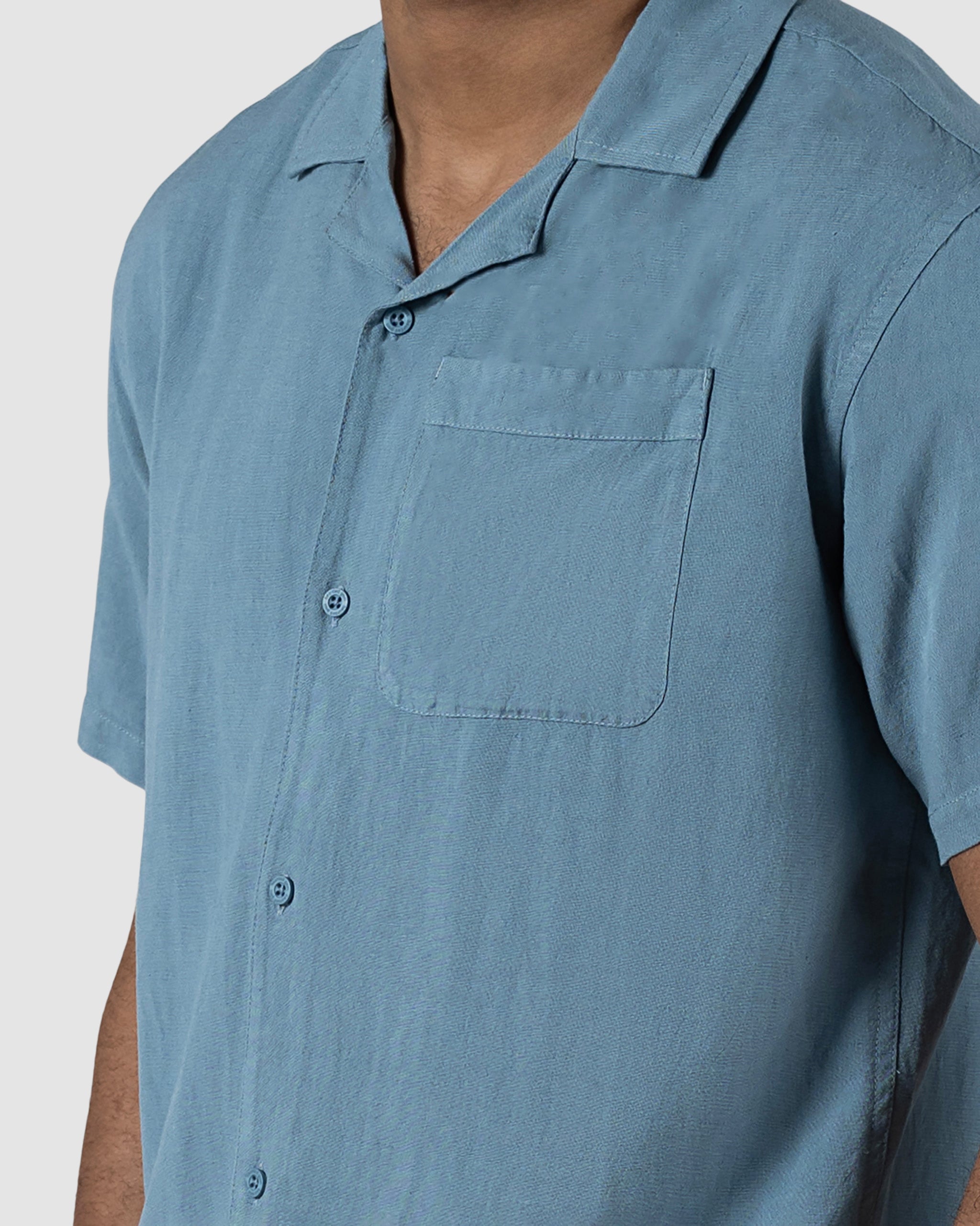 A man models the BEARDEDGOAT Mens Breeze Shirt, a lightweight, light blue short-sleeve button-up with a chest pocket, shown from shoulders to waist against a plain background.
