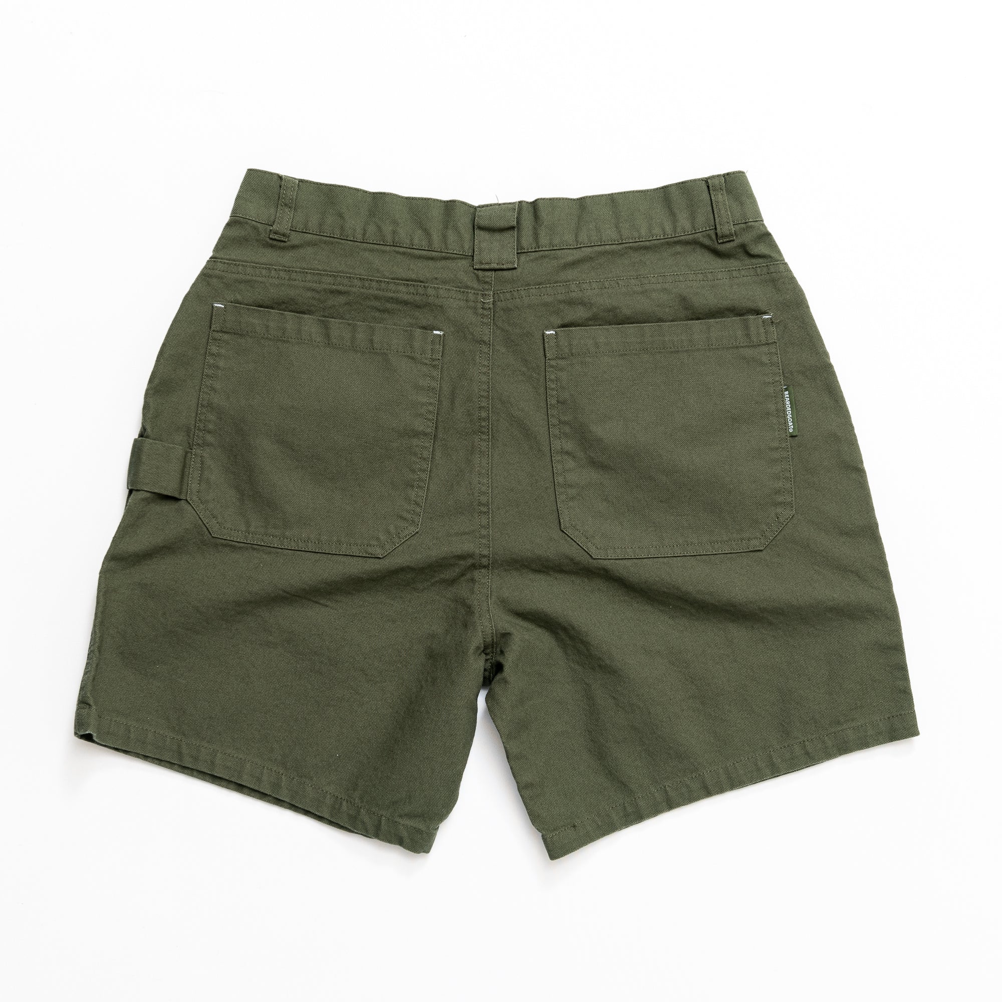 The beardedgoat Mens Foundry Short in olive green, shown flat from the back, is made from rugged cotton canvas for abrasion resistance. It features two large back pockets, a waistband belt loop, and a utility loop on the left leg.