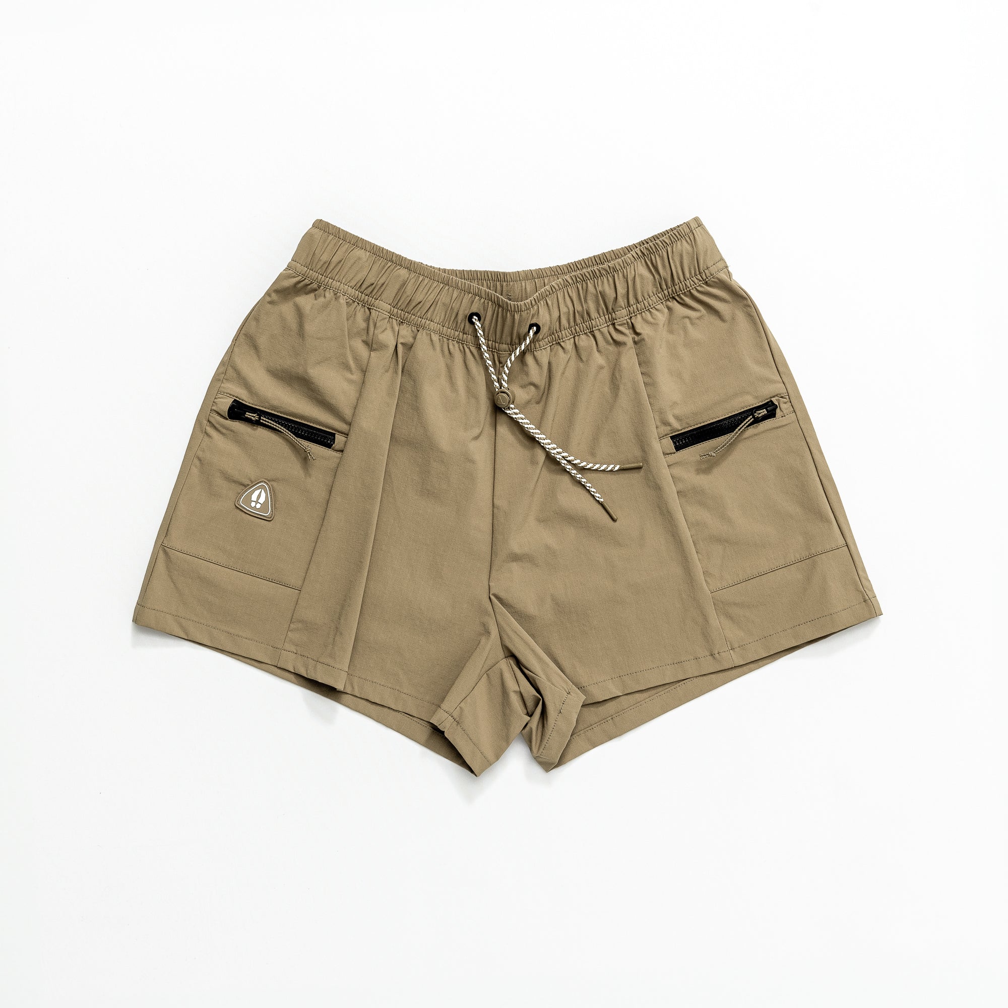 The beardedgoat Womens Summit Short in khaki features an elastic waistband, white and black drawstring, two front zip pockets, and a small triangular logo patch on the left. Made from lightweight ripstop fabric—perfect for trails. Laid flat on white background.