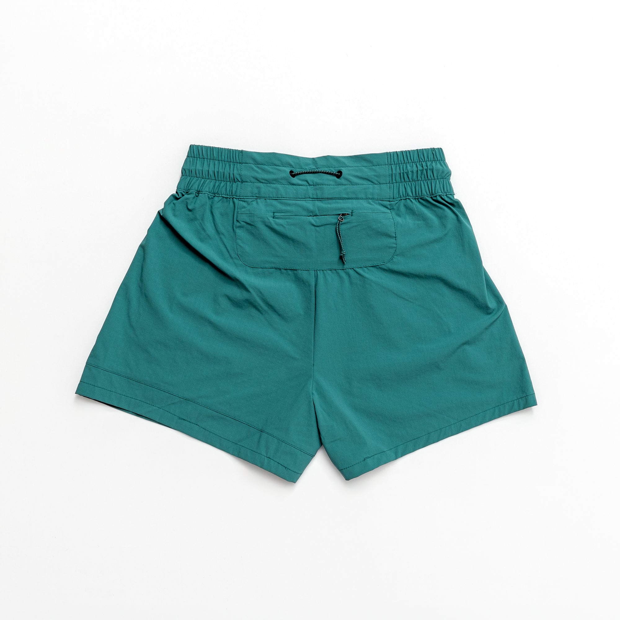 The beardedgoat Womens Alpina Short in teal green features a high-waisted fit, stretchy ripstop fabric, elastic waistband with drawstring, and zippered back pocket, shown flat on a white background.