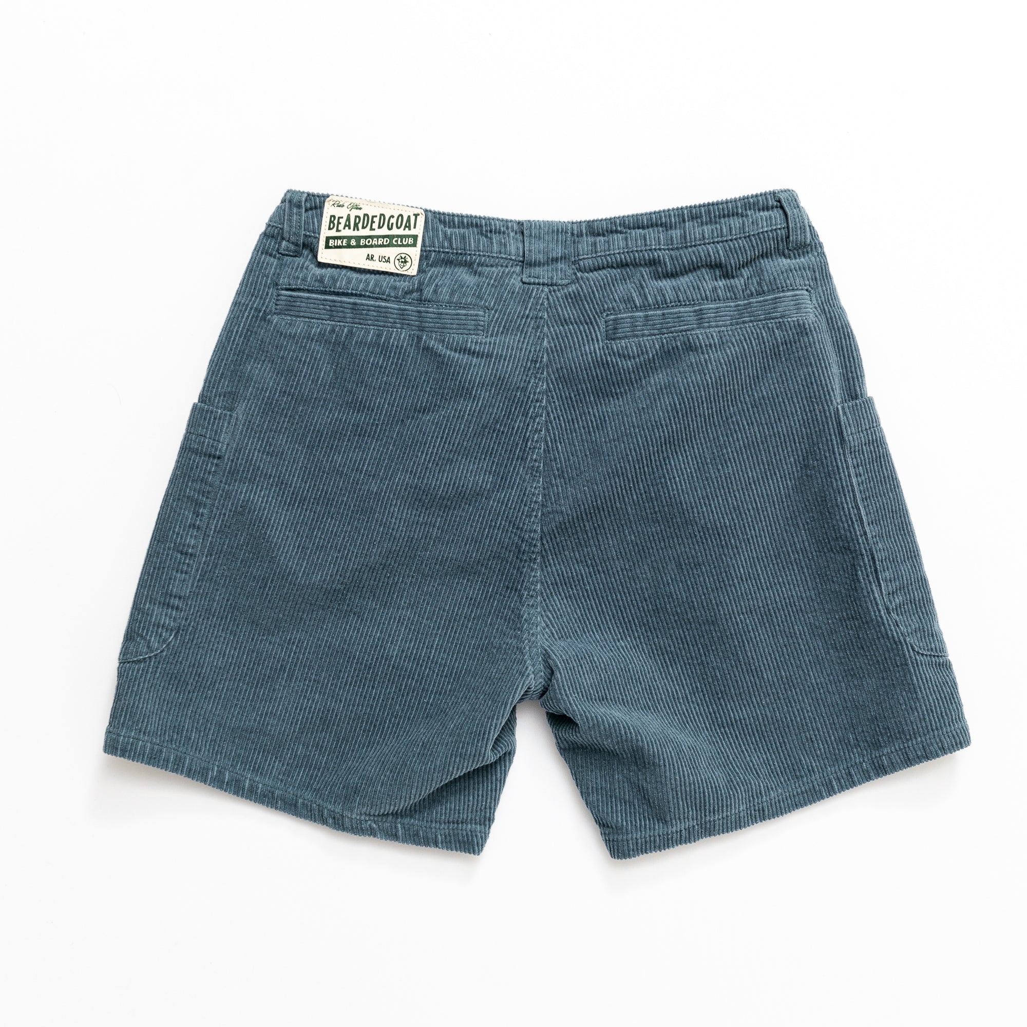 The Mens Moor Short by beardedgoat in teal blue cotton corduroy features two back pockets, side pockets, and a rectangular beardedgoat label above the right pocket—perfect for everyday casual wear.
