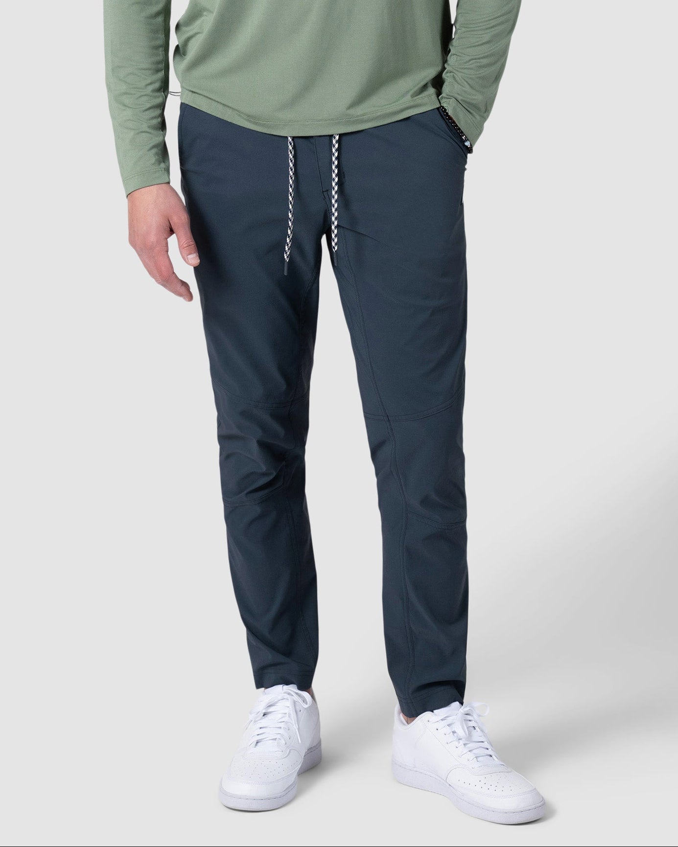 A person wearing a light green long-sleeve shirt, BEARDEDGOAT NEW-—ROVER™ Pant with a white drawstring, and white sneakers stands against a plain light background.