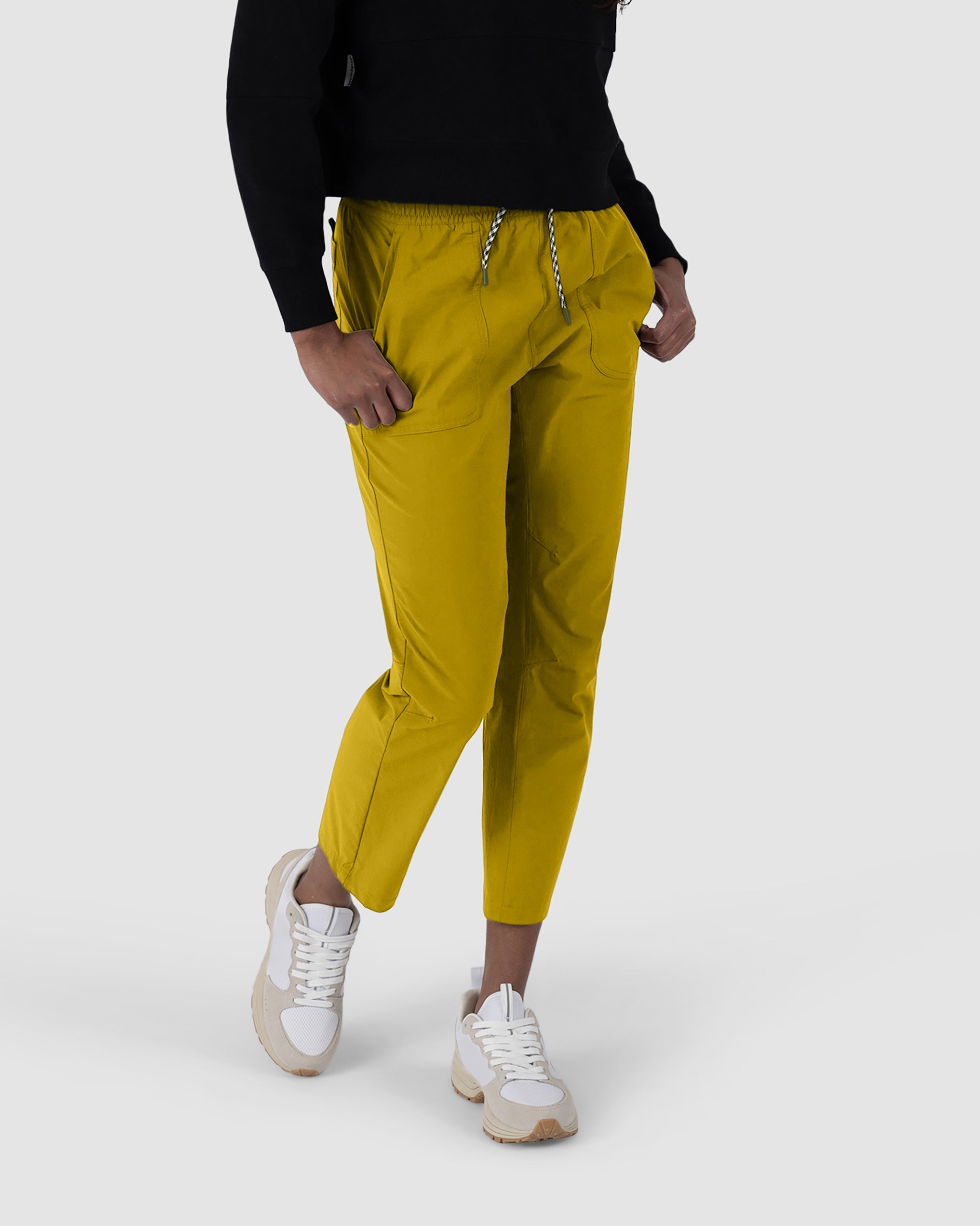 A person, head not visible, stands against a plain light gray background wearing a black top, yellow BEARDEDGOAT NEW — Summit™ Pant, and white sneakers.