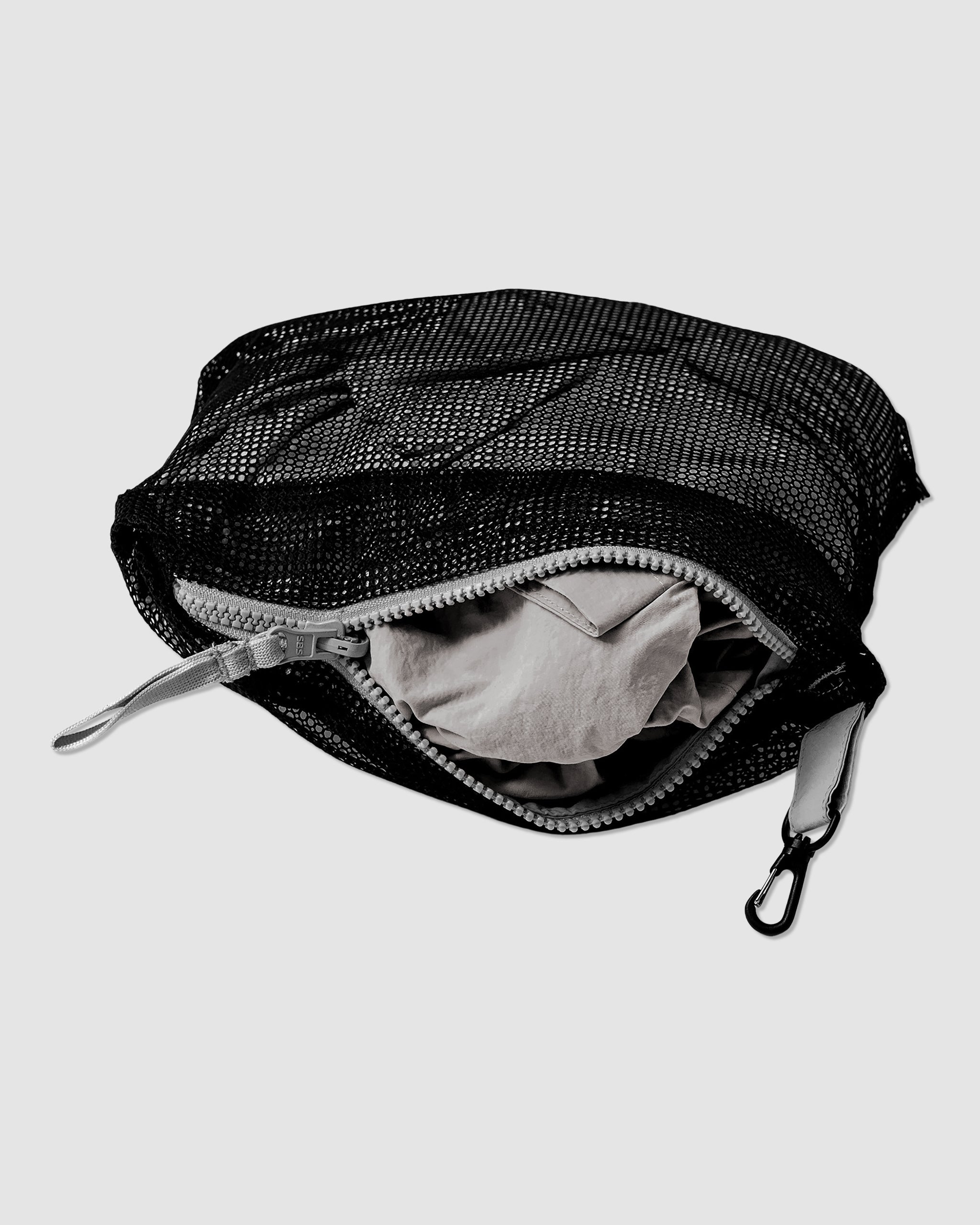 A black mesh water-resistant pouch with a light gray zipper, partially open to show a folded Womens Deluge Pullover by BEARDEDGOAT inside. The pouch also features a small black clip attached to one side.