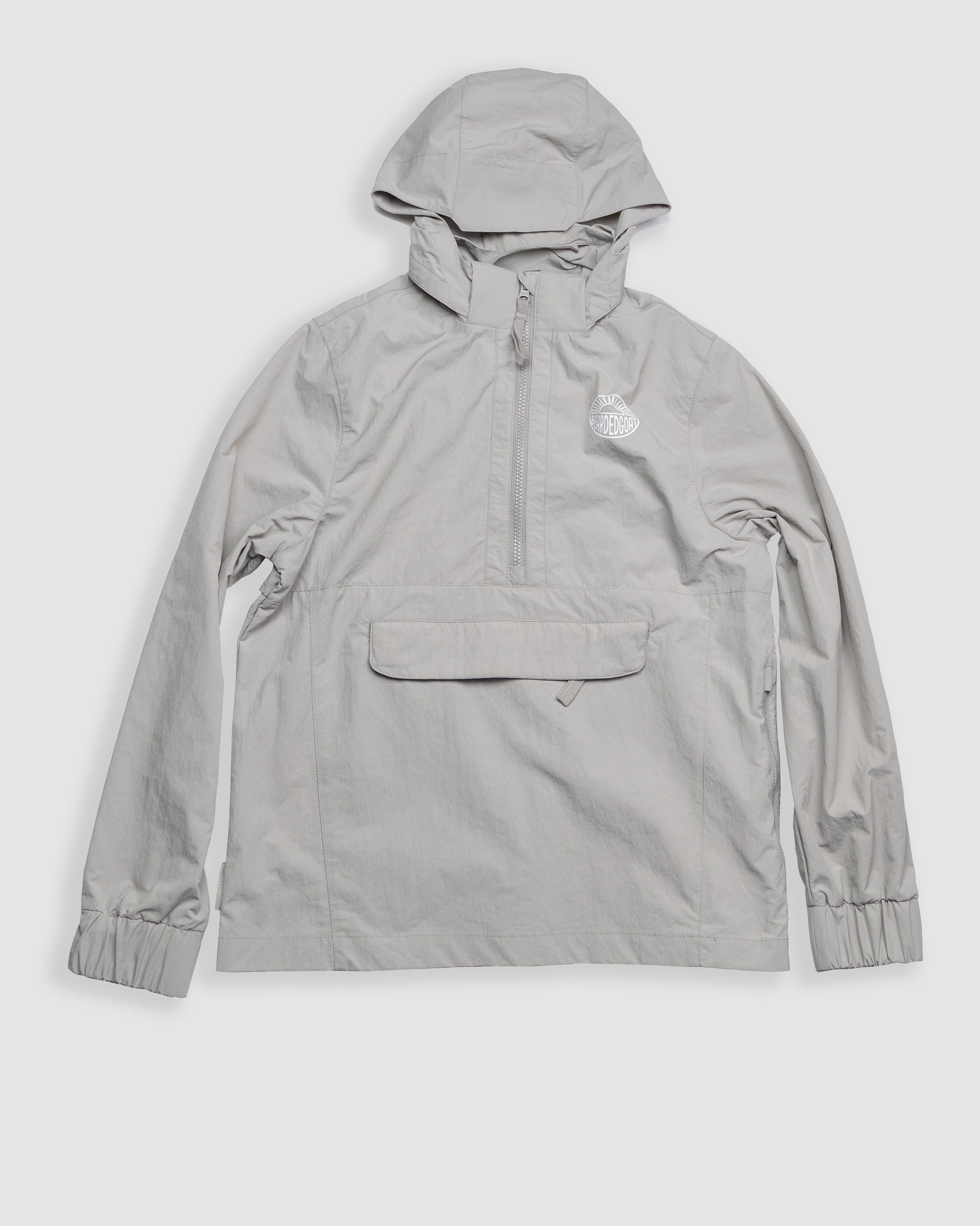 A light gray, water-resistant Womens Deluge Pullover by BEARDEDGOAT, featuring a hood, front zipper, chest pocket with flap, elastic cuffs, and the BEARDEDGOAT logo on the left chest, displayed on a plain white background.