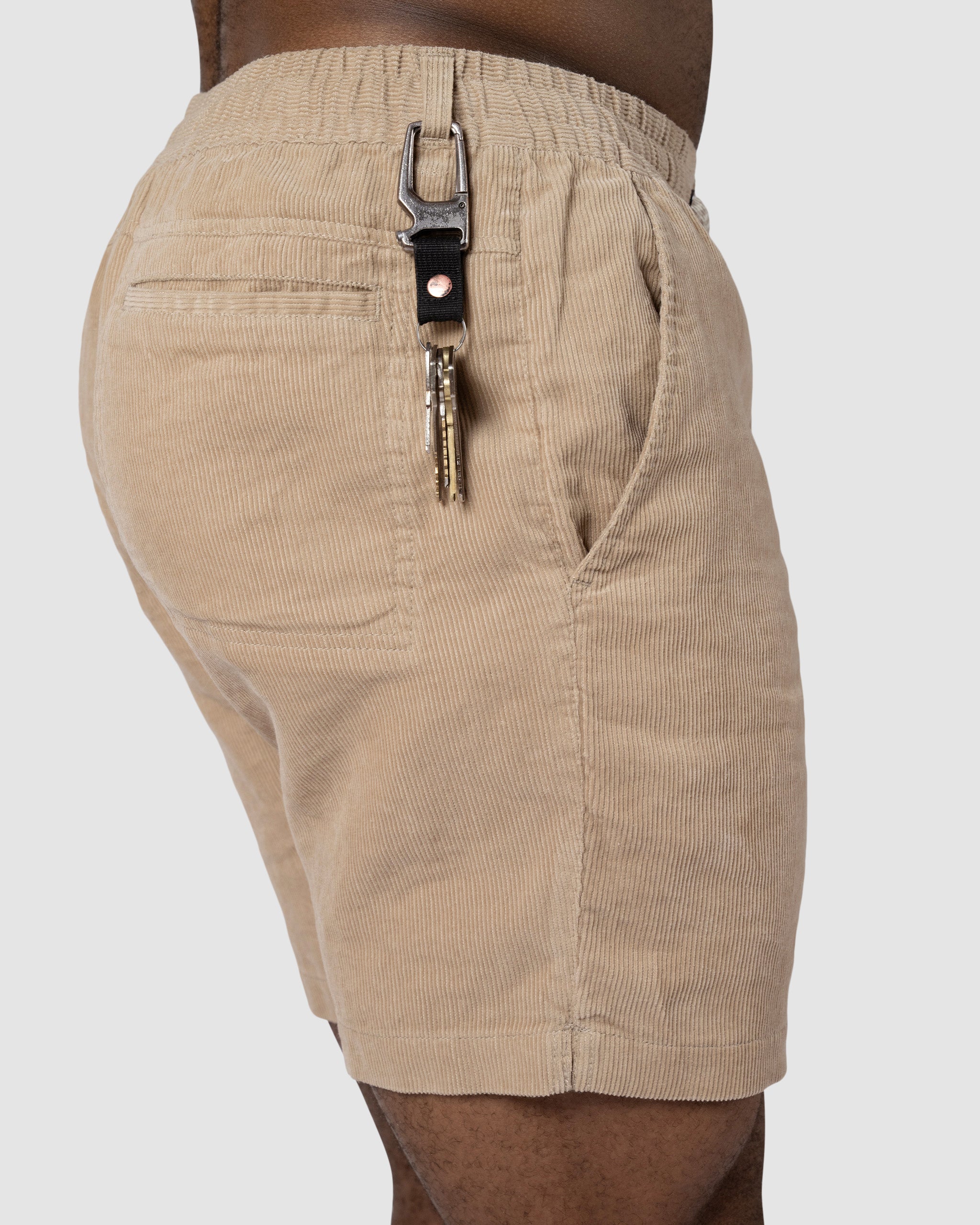 A person wearing BEARDEDGOAT Mens Cord Short with a hand in the pocket, displaying keys on a metal carabiner clipped to a belt loop—an ideal way to add vintage style to any outfit.