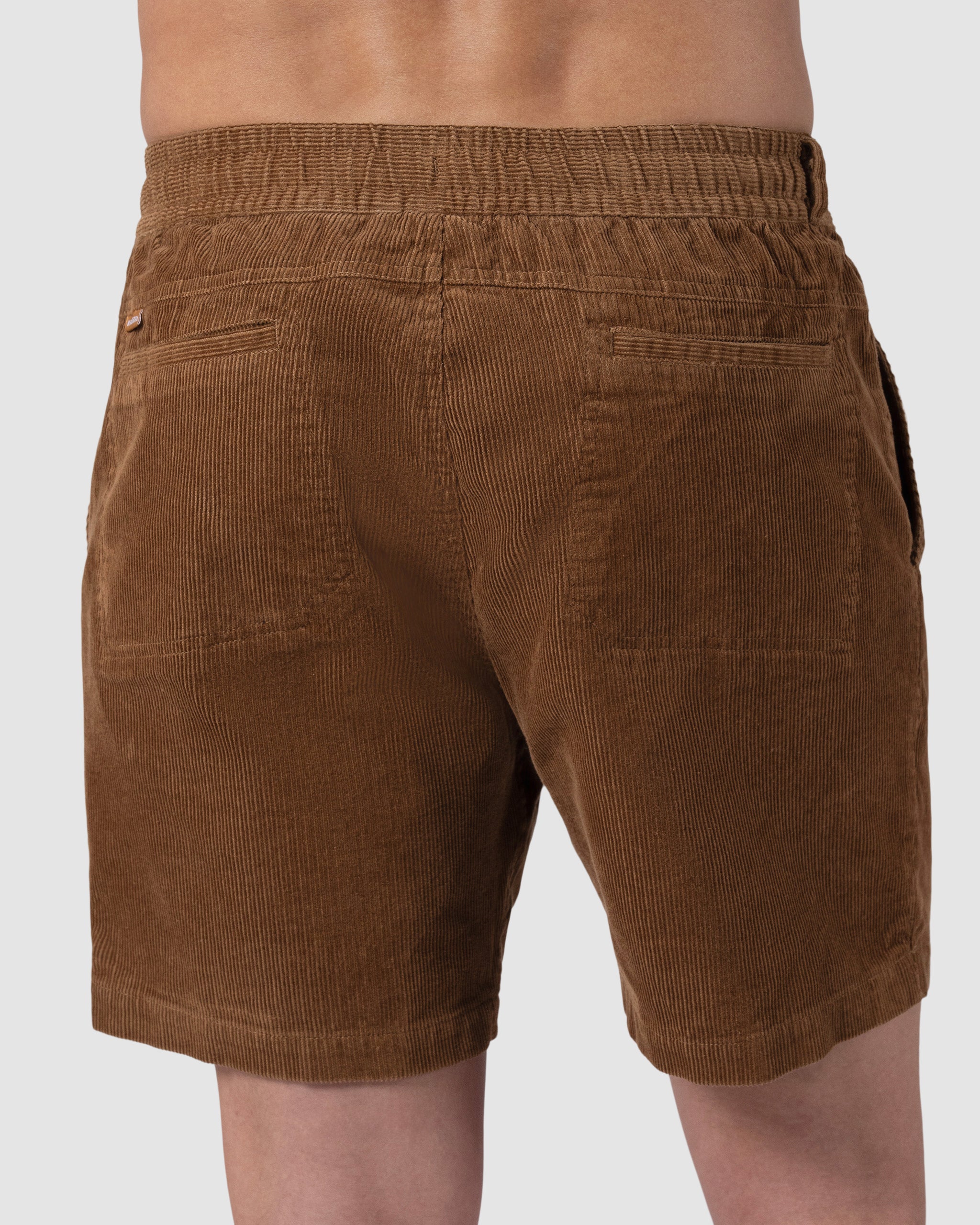 A person seen from the back wears BEARDEDGOAT Mens Cord Short in brown, featuring an elastic waistband, two back pockets, and ribbed textured fabric for a vintage look.