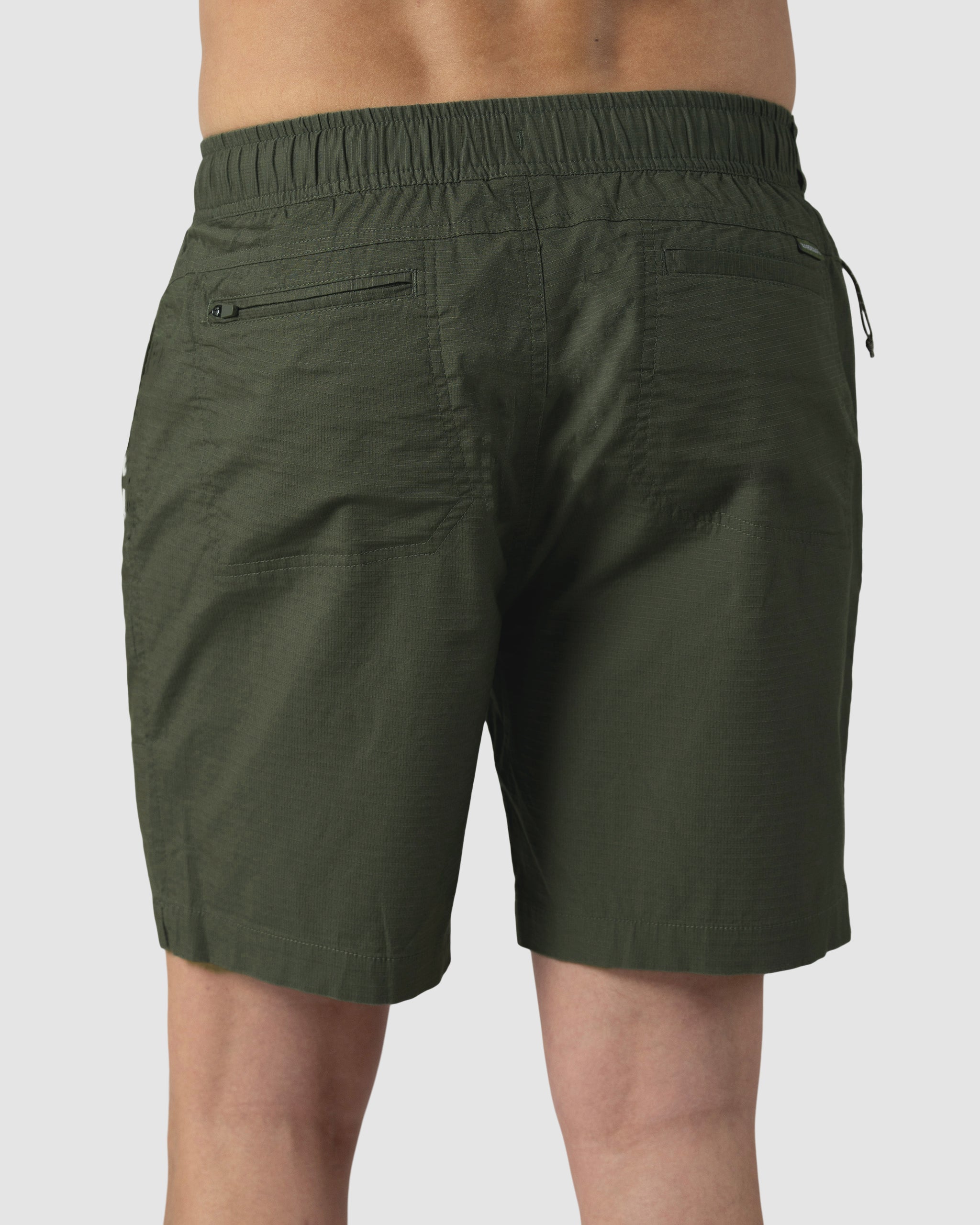 A person wears the BEARDEDGOAT Mens Canopy Short in dark green, crafted from lightweight stretch cotton ripstop with a textured finish, elastic waistband, and practical back pockets, shown from the back.