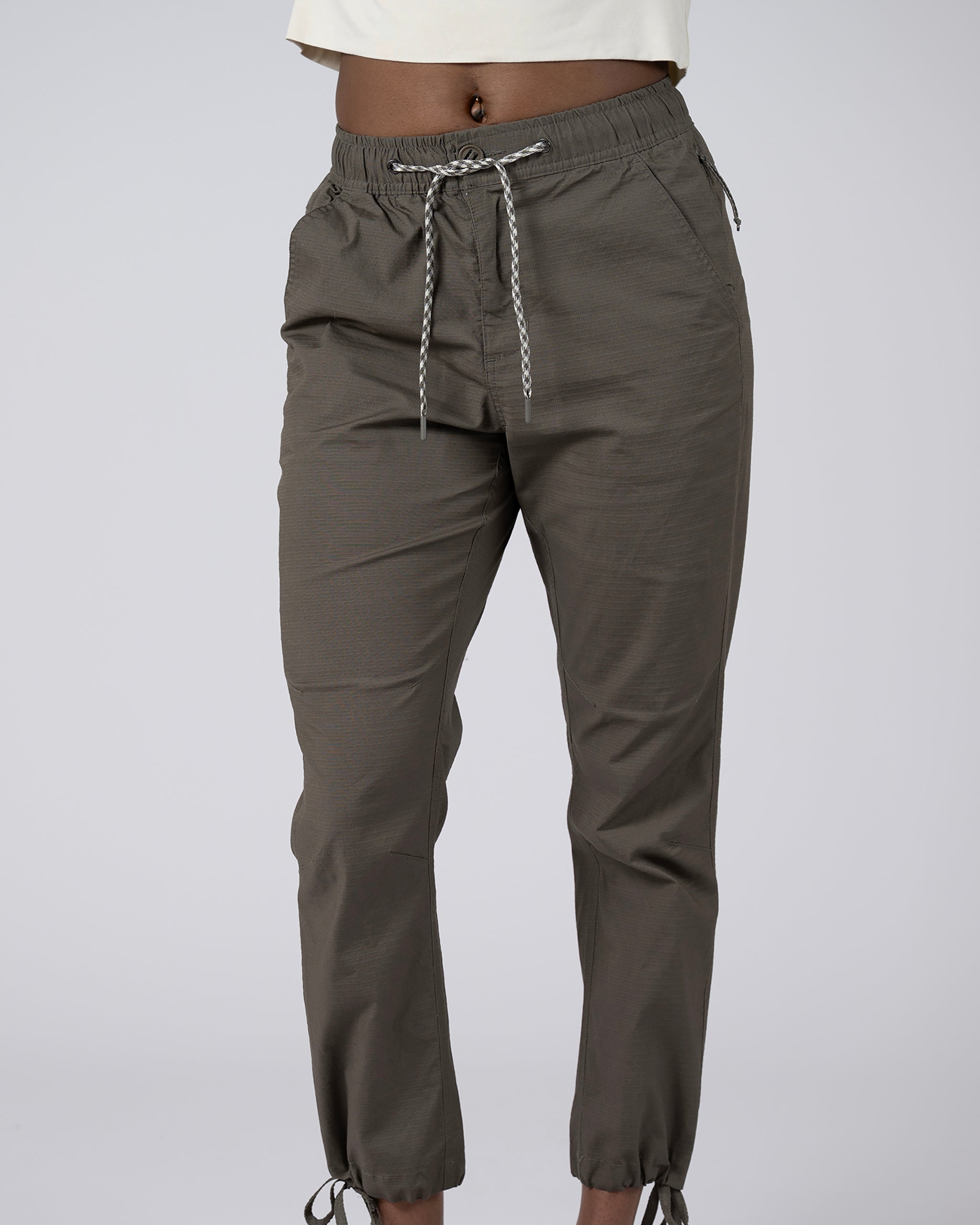 A person wears BEARDEDGOAT Women's Canopy™ Pant in Bungee Cord, featuring stretch cotton ripstop, an elastic waistband, and adjustable ankle drawcords; only the lower torso and legs are shown against a plain background.