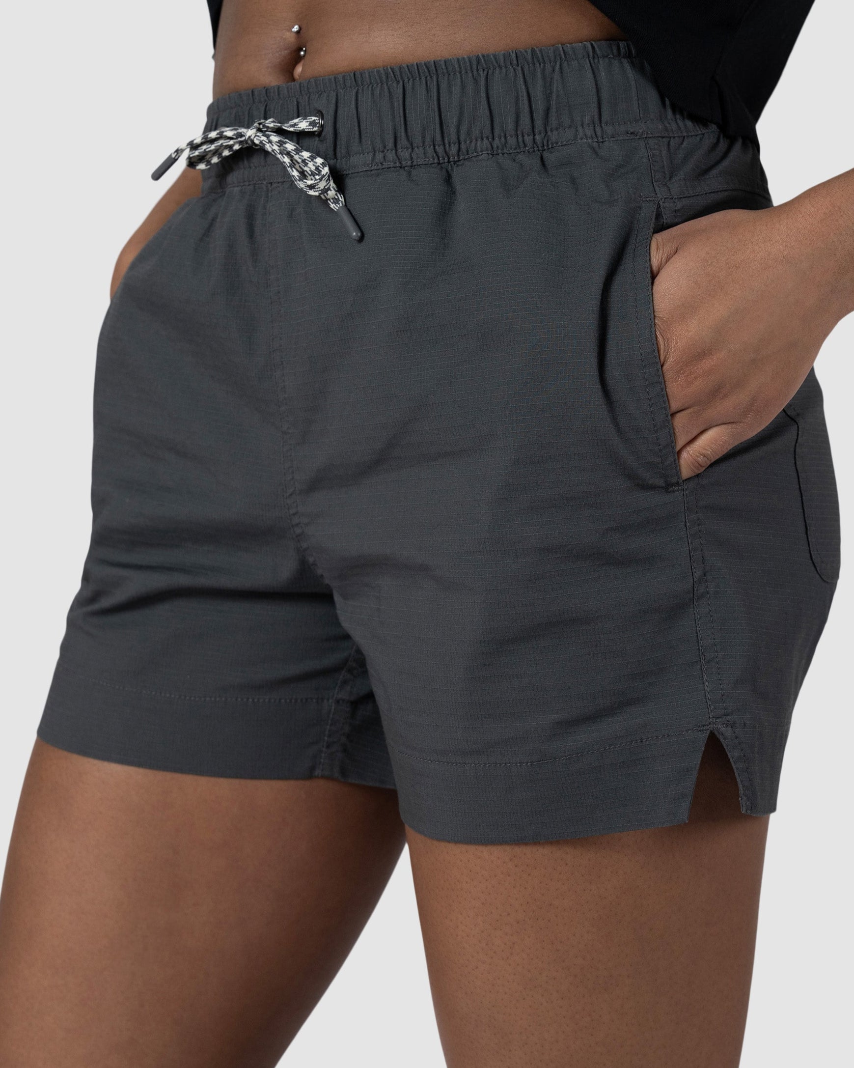 A woman wears the BEARDEDGOAT Womens Canopy Short in dark gray stretch cotton ripstop with side pockets and a small side slit. Only the waist to mid-thigh is visible against a plain background.