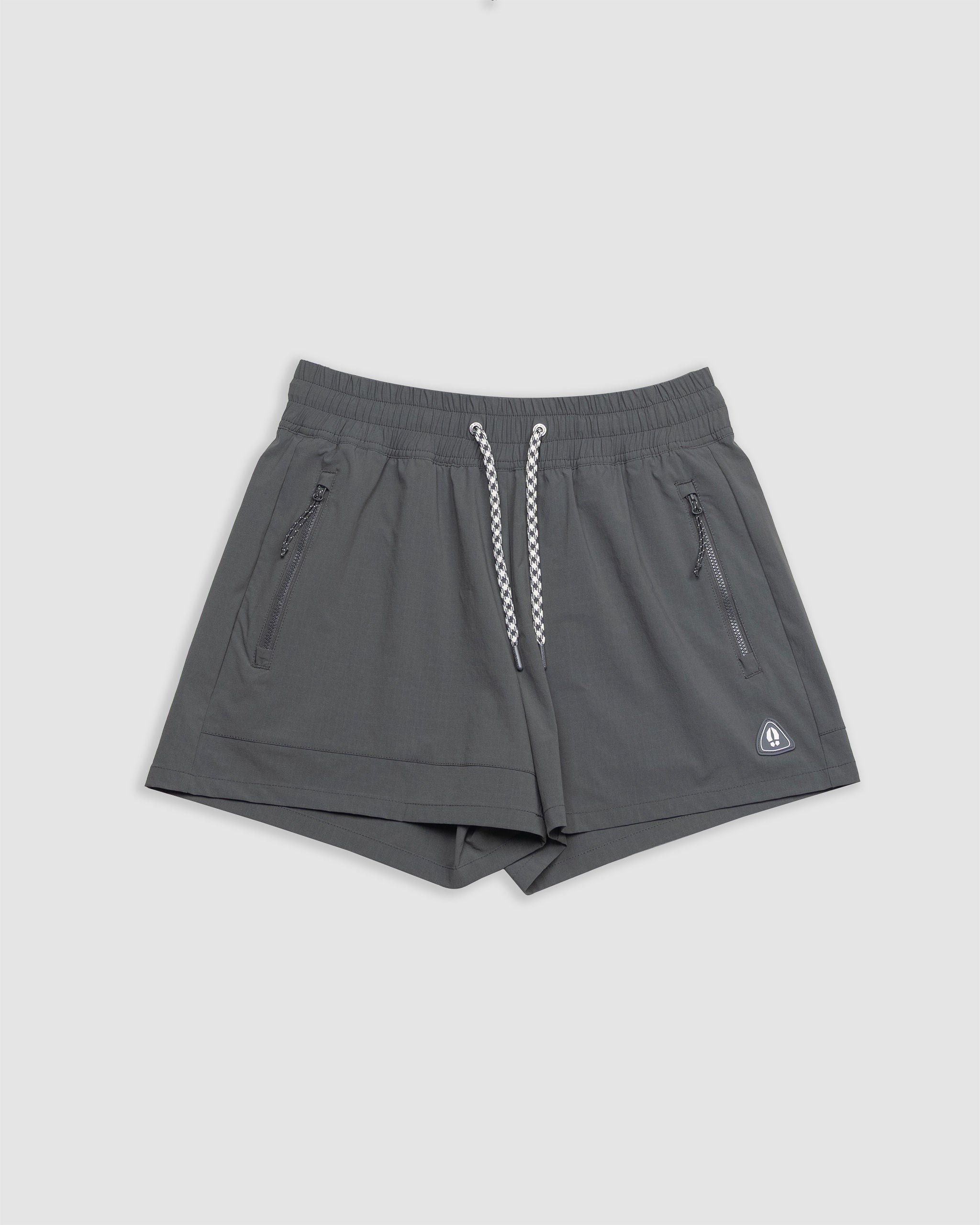 The BEARDEDGOAT Women's Alpina Short in dark shadow features a high waist, elastic waistband with white drawstrings, two zippered side pockets, and a small triangular logo on the left leg, shown laid flat on a light gray background.