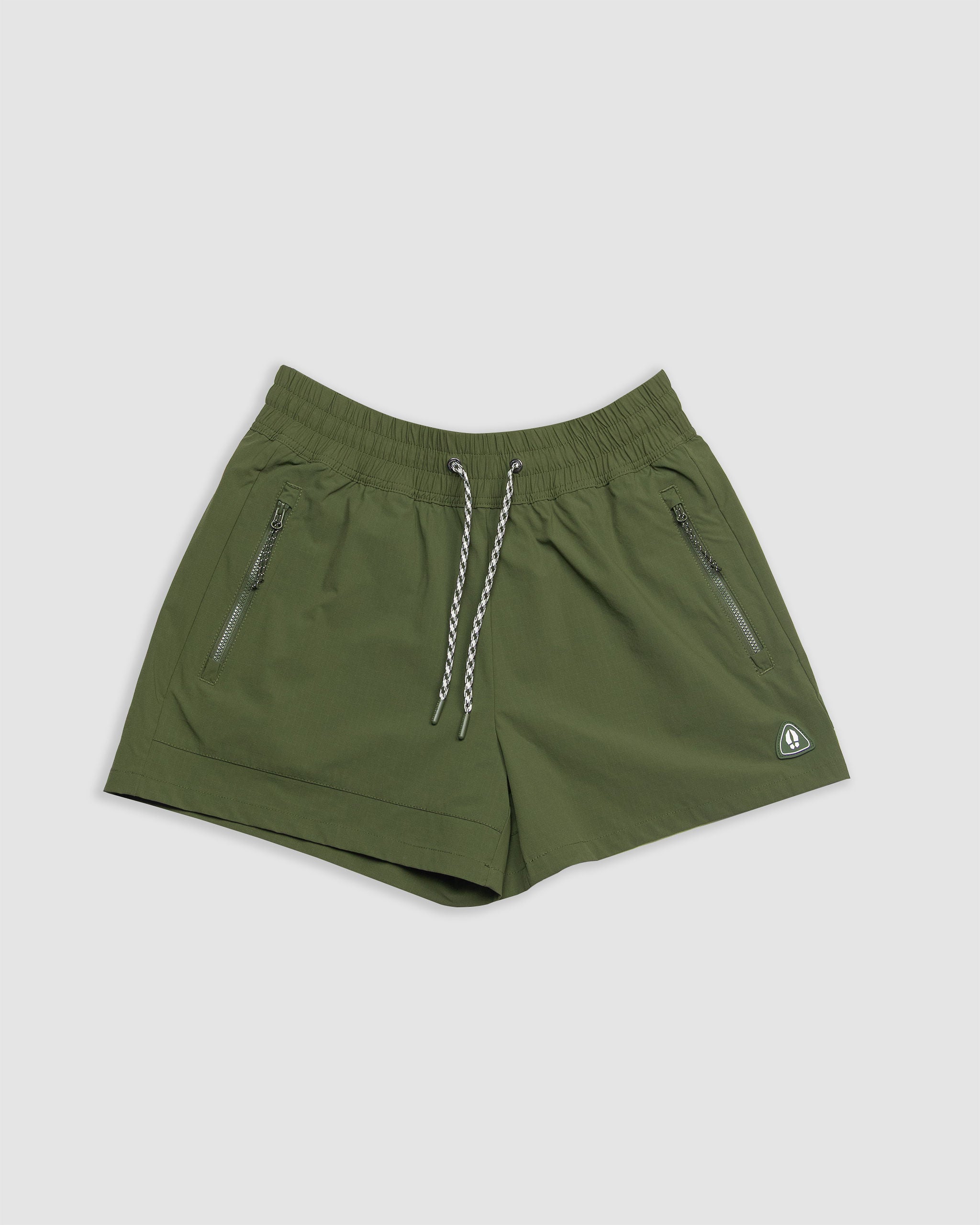 The BEARDEDGOAT Women's Alpina Short in olive green features a high waist, elastic waistband, white and gray drawstring, two front zippered pockets, and a small white logo on the lower left side, shown on a plain light background.