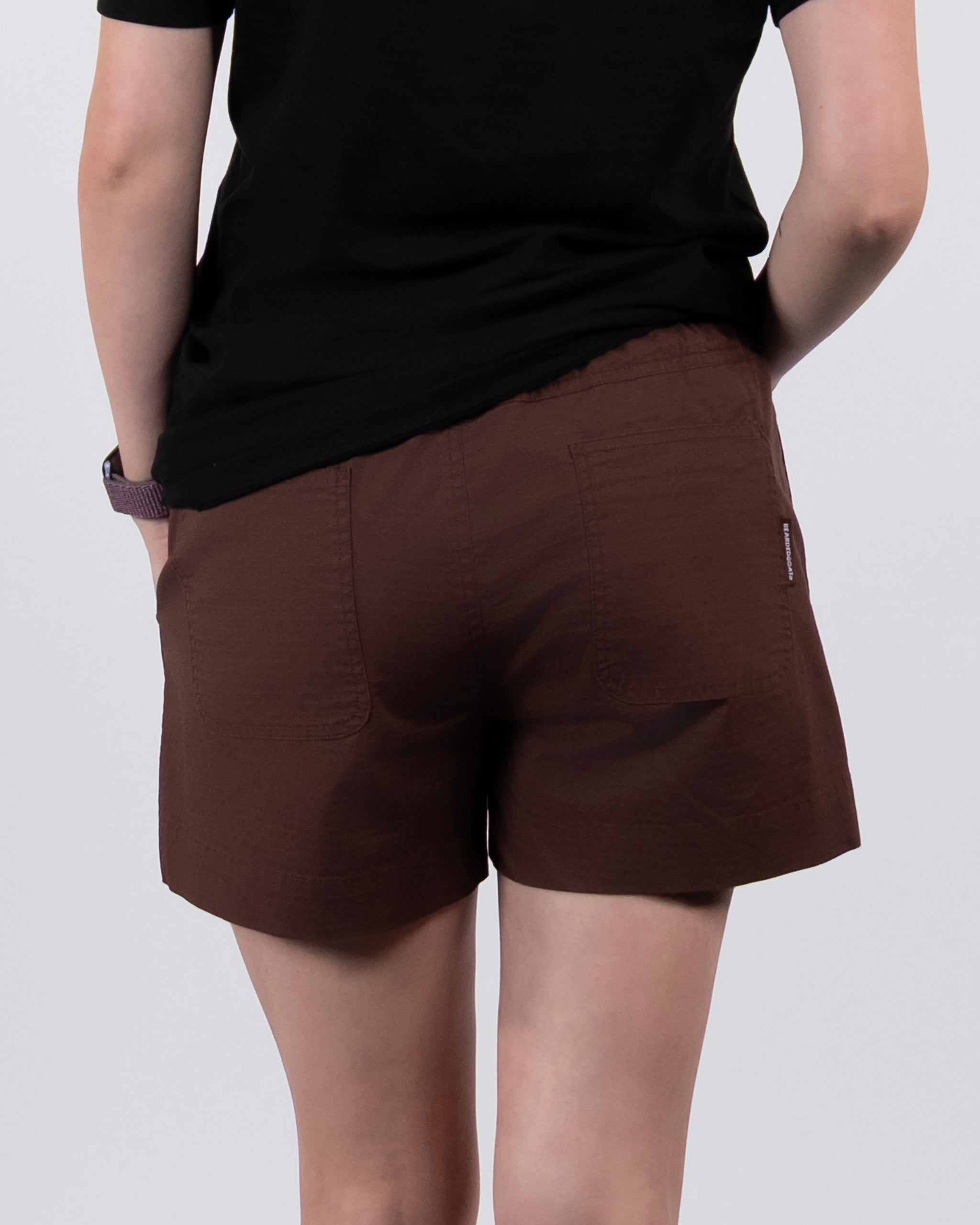 A person is seen from behind wearing a black shirt and BEARDEDGOAT Women's Canopy Short in brown stretch cotton ripstop, showcasing the rear view of the outfit.