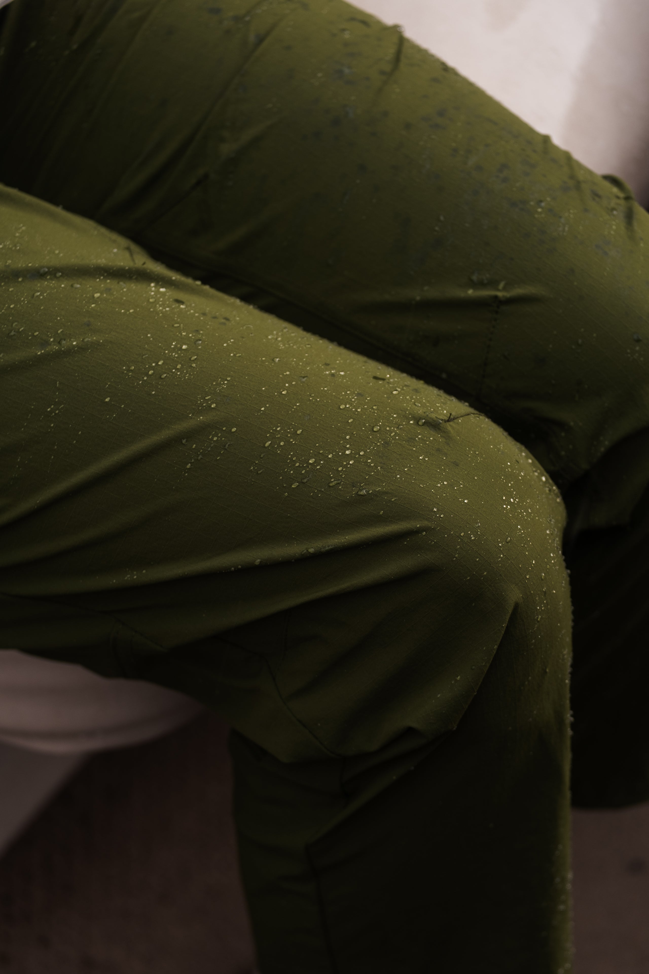 A close-up of someone wearing BEARDEDGOAT’s NEW — Summit™ Pant in olive green, with small water droplets on the women’s performance fabric.