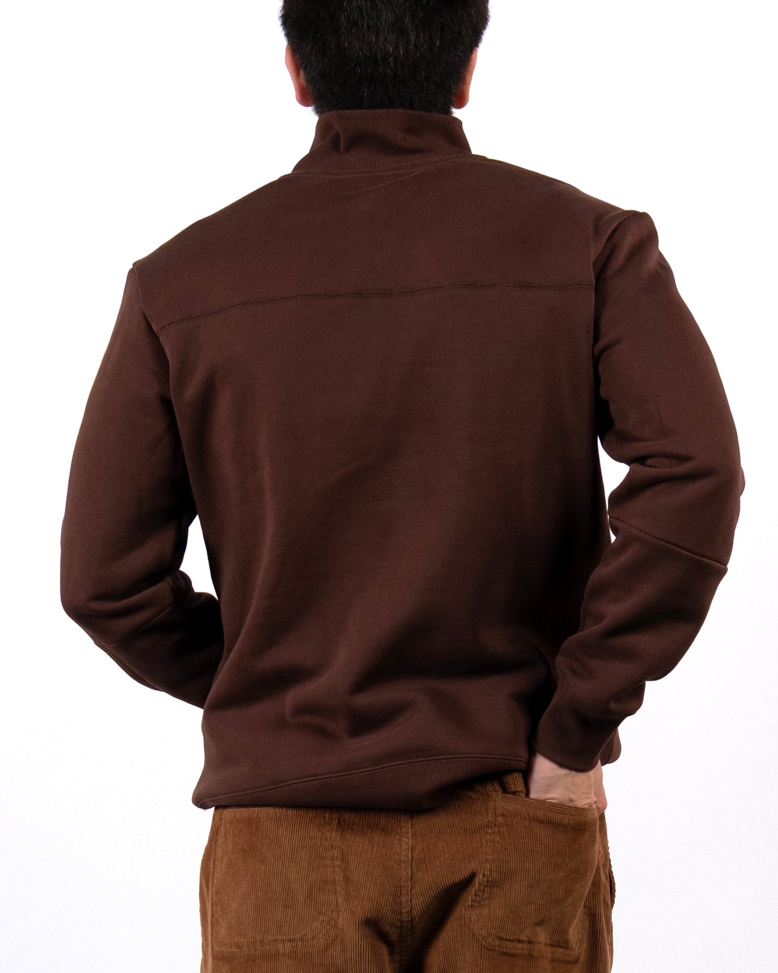 A person stands with their back to the camera, wearing the BEARDEDGOAT NEW — VOID™ Half Zip in brown premium cotton fleece against a plain white background.