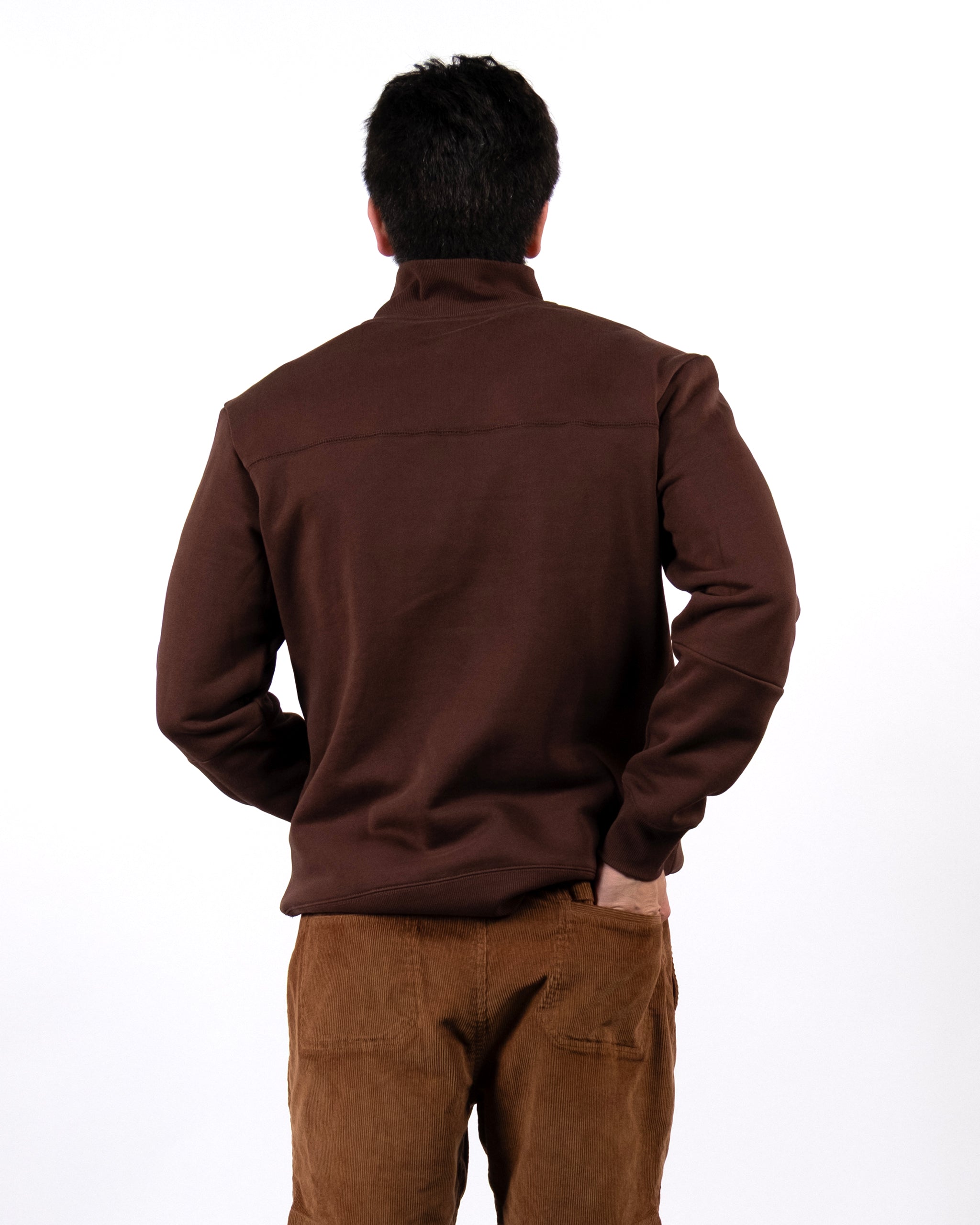 A person stands with their back to the camera, wearing the BEARDEDGOAT NEW — VOID™ Half Zip in brown premium cotton fleece against a plain white background.
