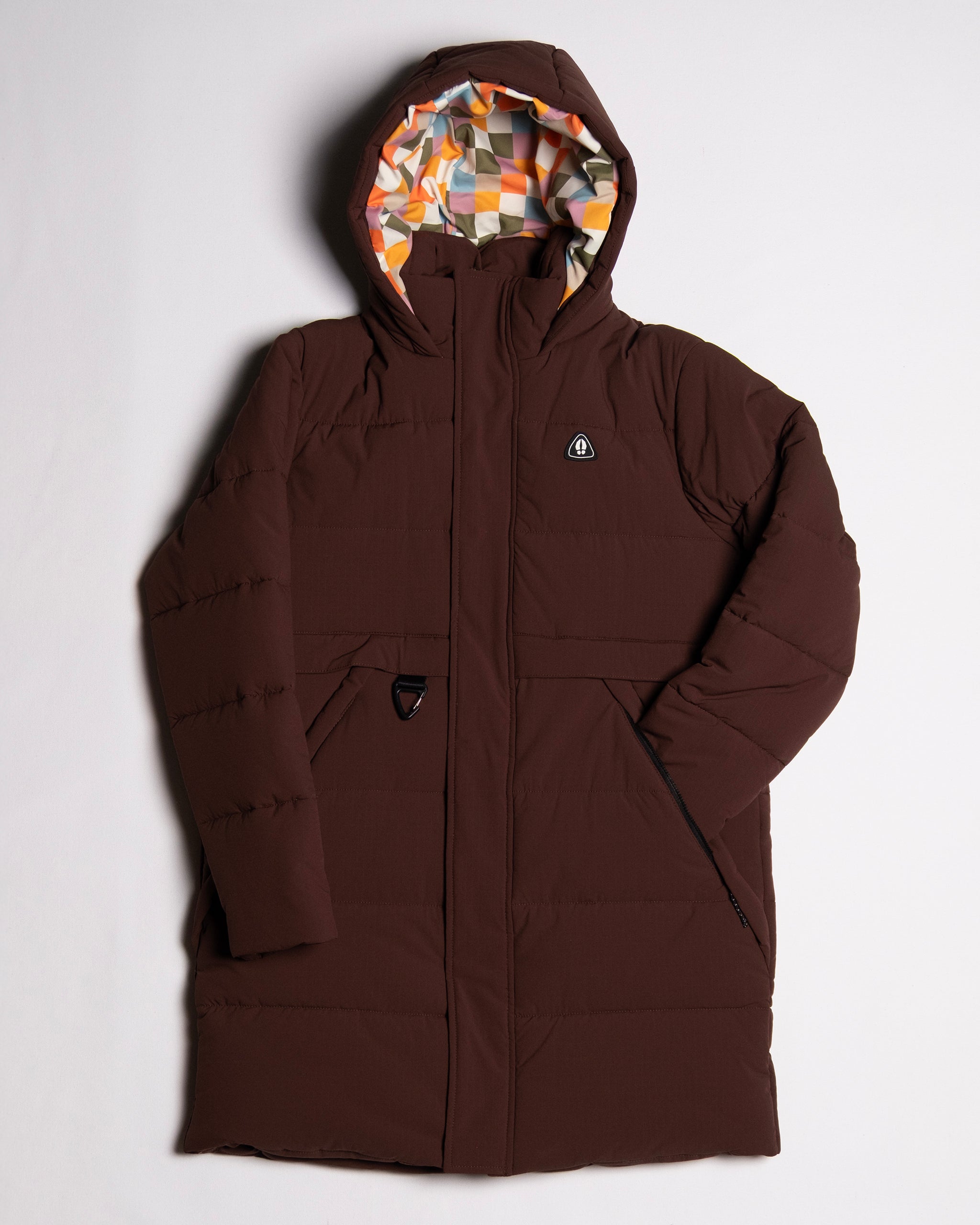 The beardedgoat NEW — MERIDIAN™ PARKA is a limited edition long brown winter coat with a hood, colorful geometric-patterned lining, synthetic down insulation, front zipper, and two front pockets, shown on a plain white background.