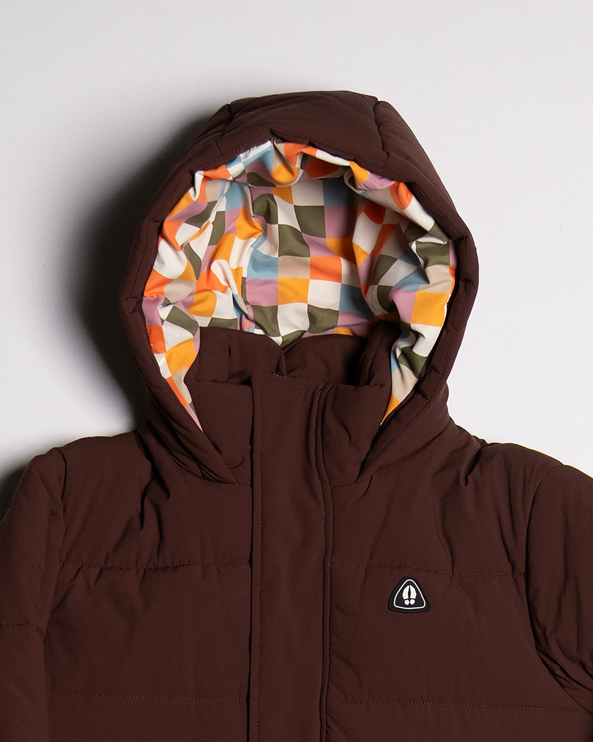 The NEW — MERIDIAN™ PARKA by beardedgoat is a limited edition brown hooded parka with synthetic down, featuring a multicolored orange, yellow, green, and white checkered lining and a small triangular chest logo.