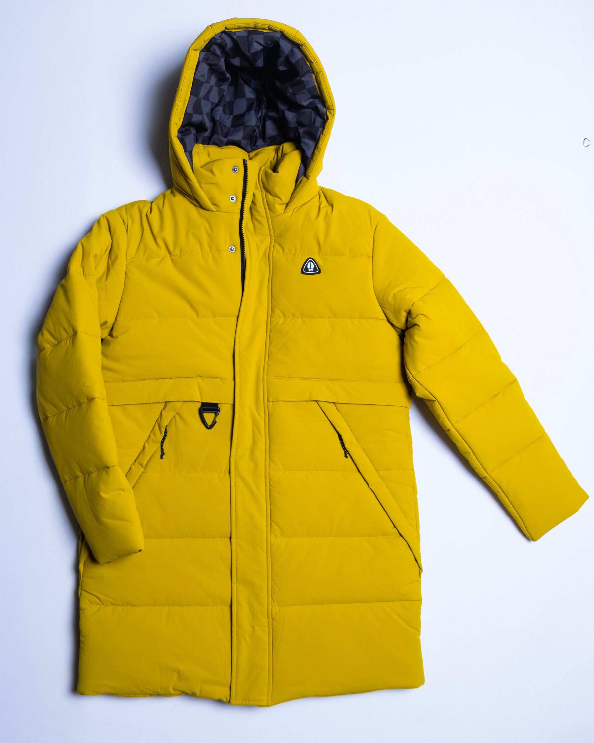 The NEW — MERIDIAN™ PARKA by beardedgoat is a long, bright yellow synthetic down parka with a hood, black geometric-pattern lining, two front zip pockets, and a small black logo patch on the chest, shown laid flat on white.