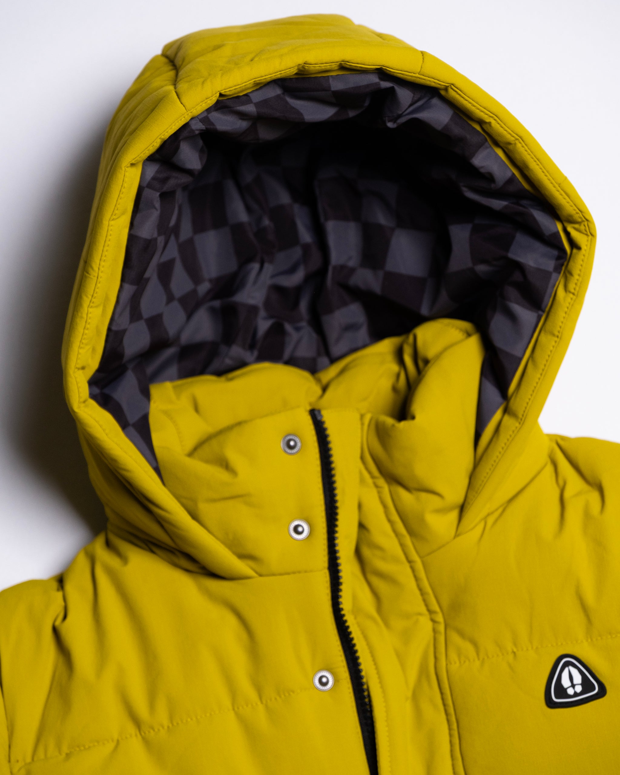 The beardedgoat NEW — MERIDIAN™ PARKA is a yellow hooded winter jacket with a black and gray geometric inner lining, snap buttons, a zipper, and a small triangular chest logo. Limited edition.