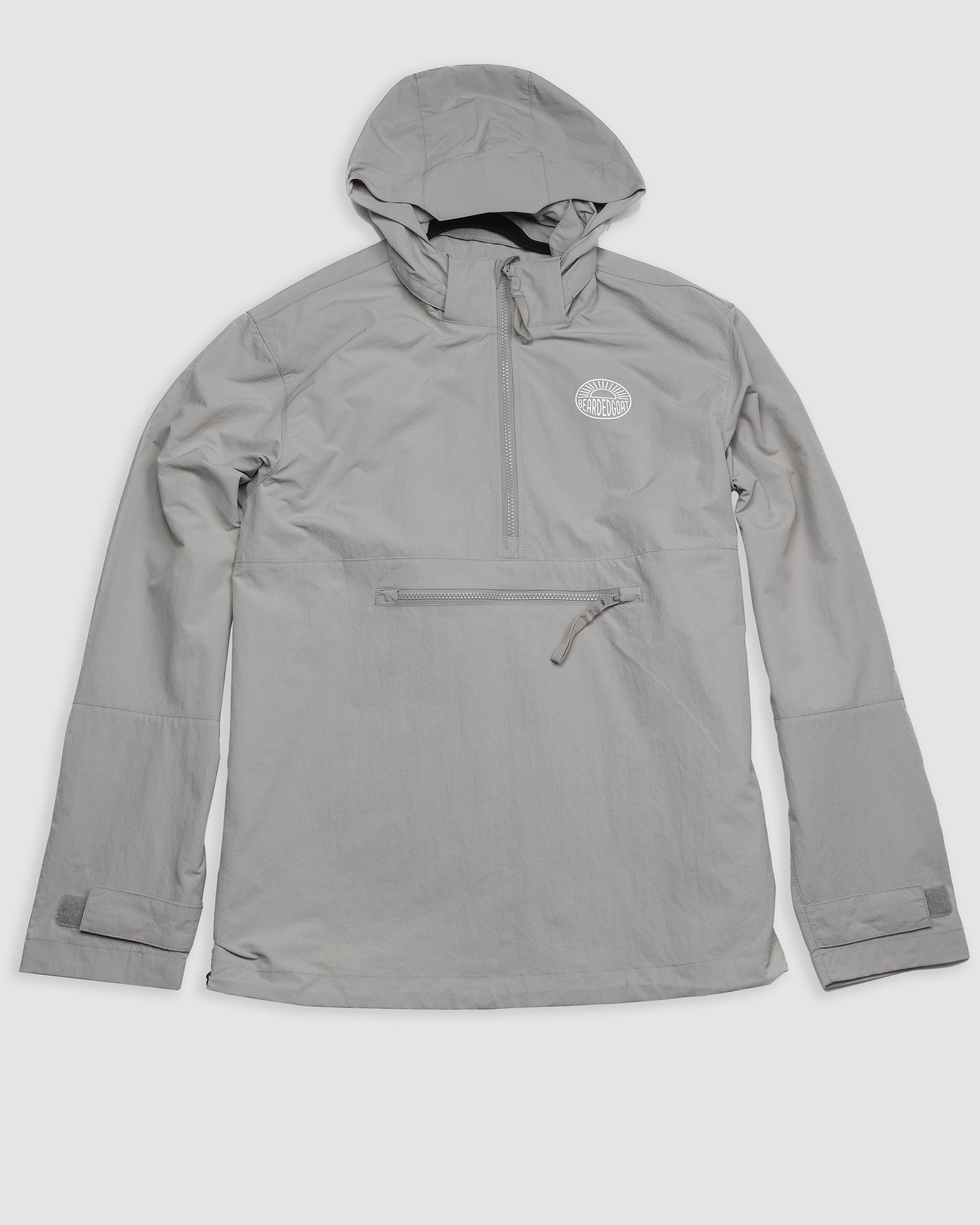The BEARDEDGOAT Mens Deluge Pullover is a lightweight, light gray half-zip hooded jacket with a zippered front pocket, adjustable wrist straps, small circular white chest logo, and water-resistant, packable design—shown on a plain white background.