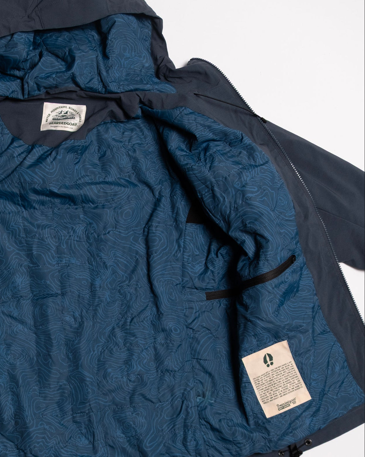 The NEW — OSLO Rover™ Performance All-Season Jacket by beardedgoat is shown open, revealing a blue topographic map lining and two white labels with black text sewn into this versatile all-season navy blue jacket.