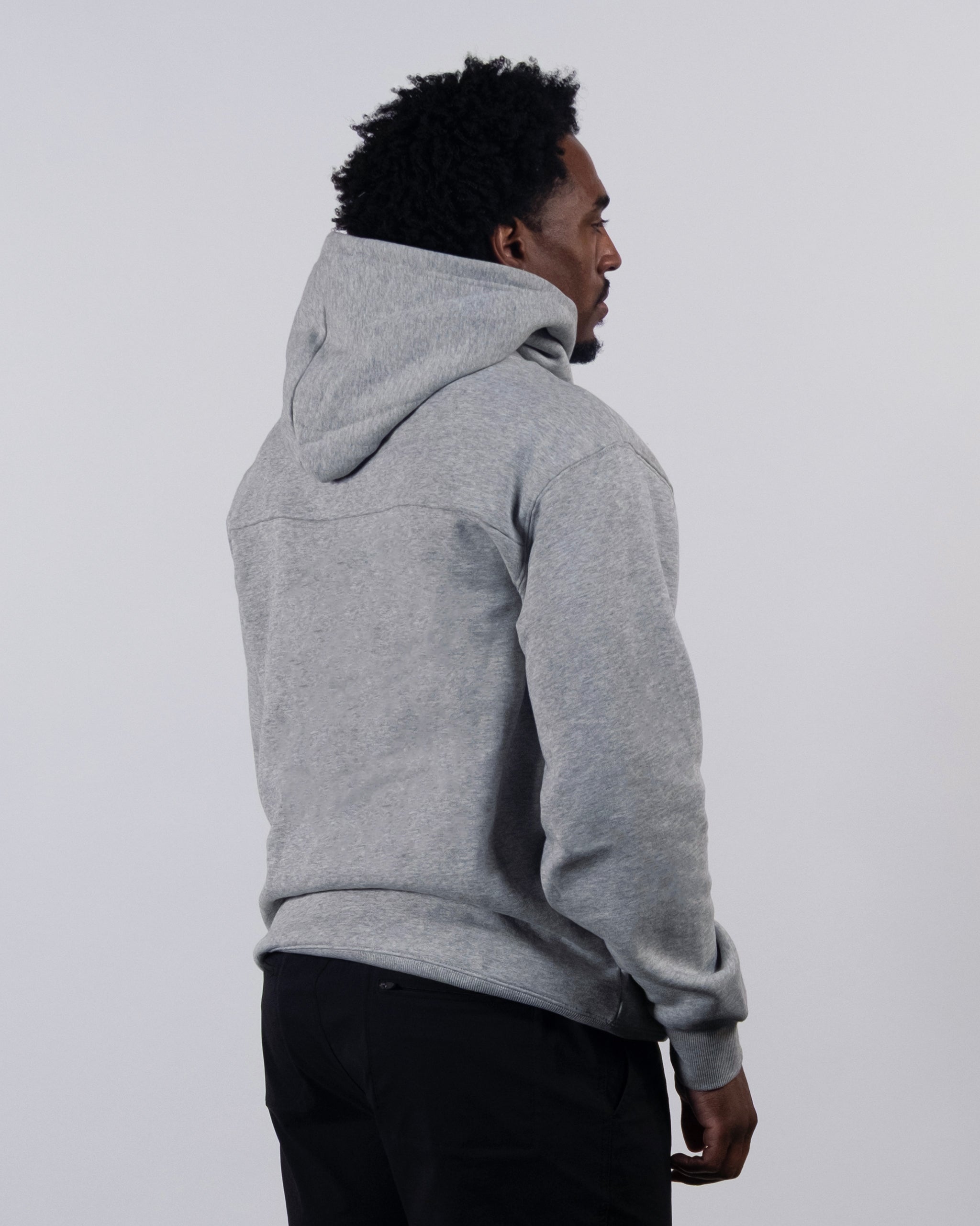A person in a beardedgoat The VOID™ Hoodie made from heavyweight cotton fleece and black pants stands angled away, head turned slightly to the side, against a plain light-colored background.