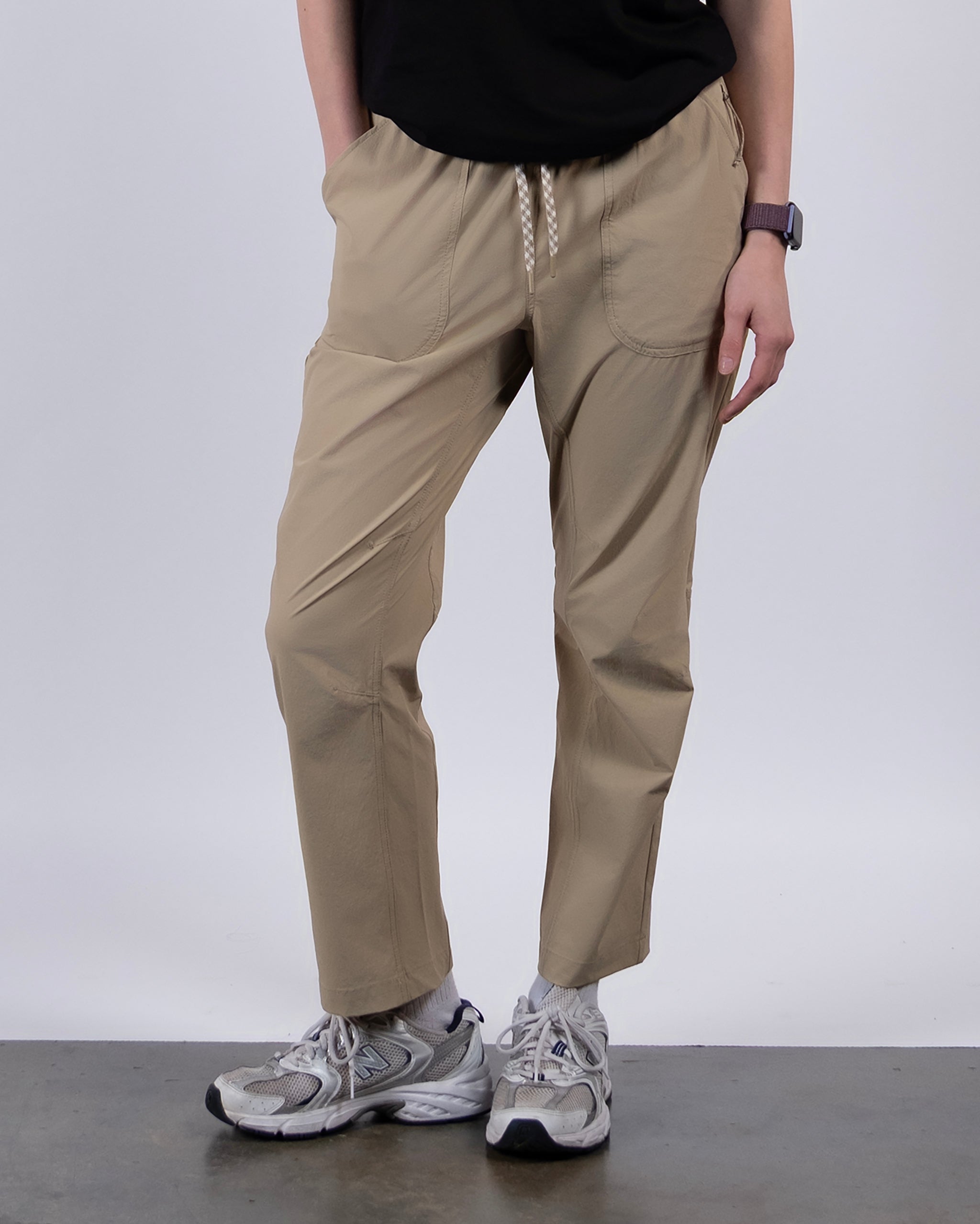 A person models the BEARDEDGOAT NEW — Summit™ Pant in beige, paired with a black shirt, gray athletic shoes, and a watch. Hands are in pockets; only the lower and part of the upper body are visible against a light background.