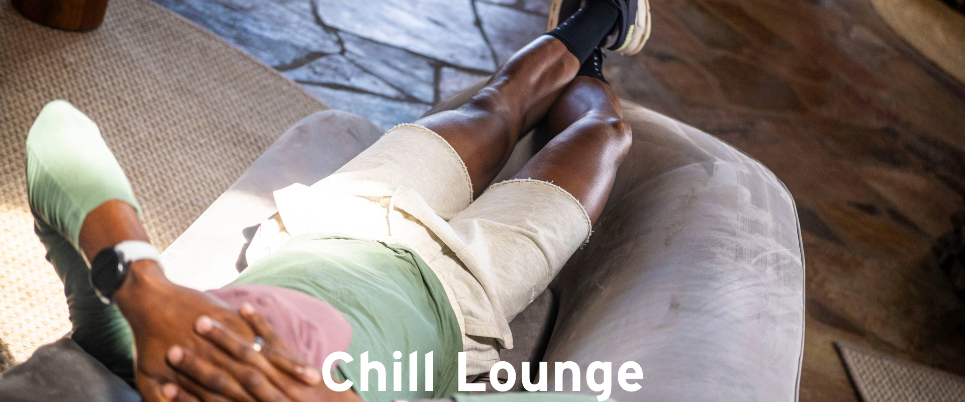 A person wearing a green shirt and beige shorts relaxes on a gray couch with hands behind their head. The words Chill Lounge appear at the bottom of the image.