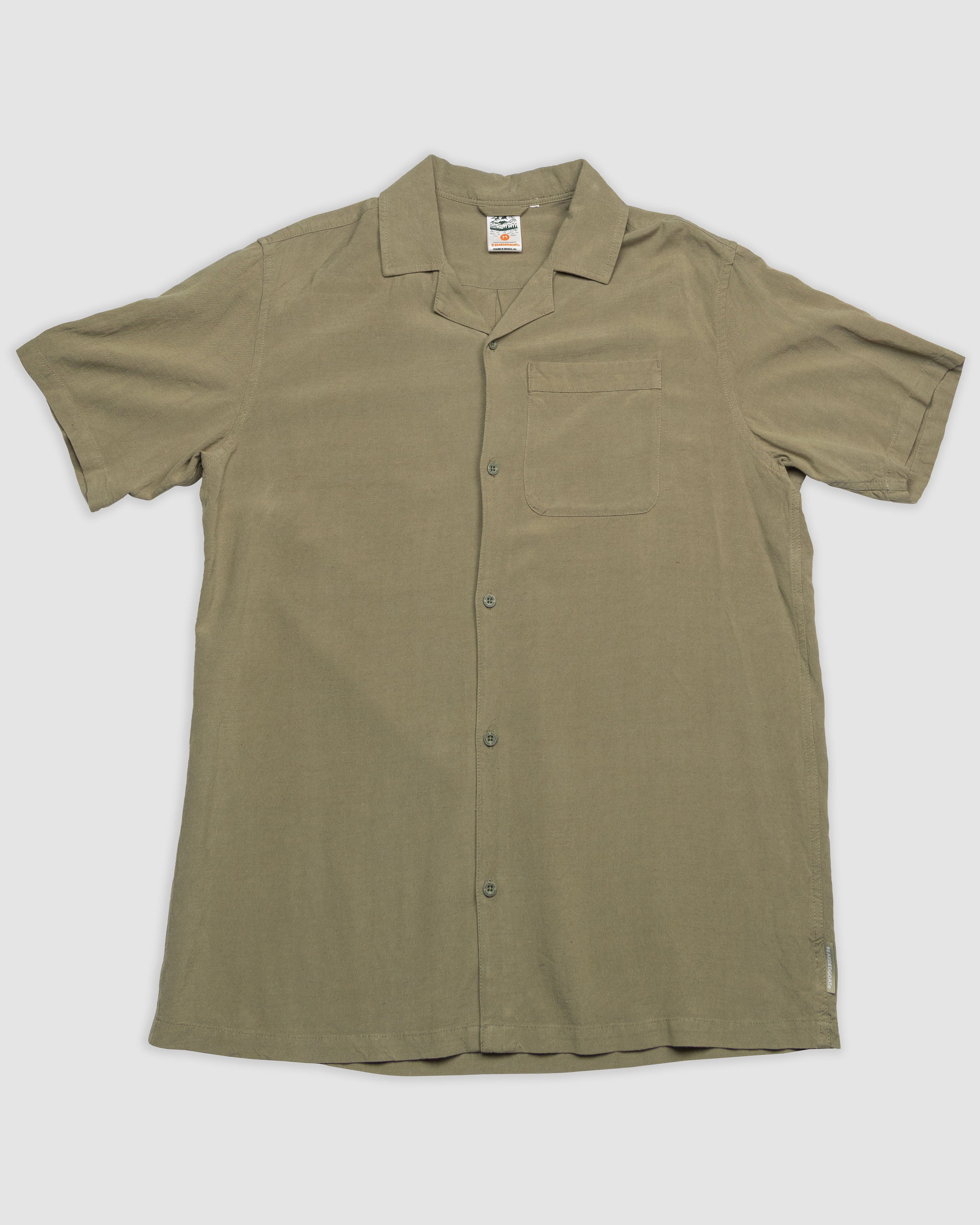 The BEARDEDGOAT Mens Breeze Shirt is a lightweight olive green linen button-up with short sleeves, a notched collar, and a single chest pocket, shown laid flat on a light background.