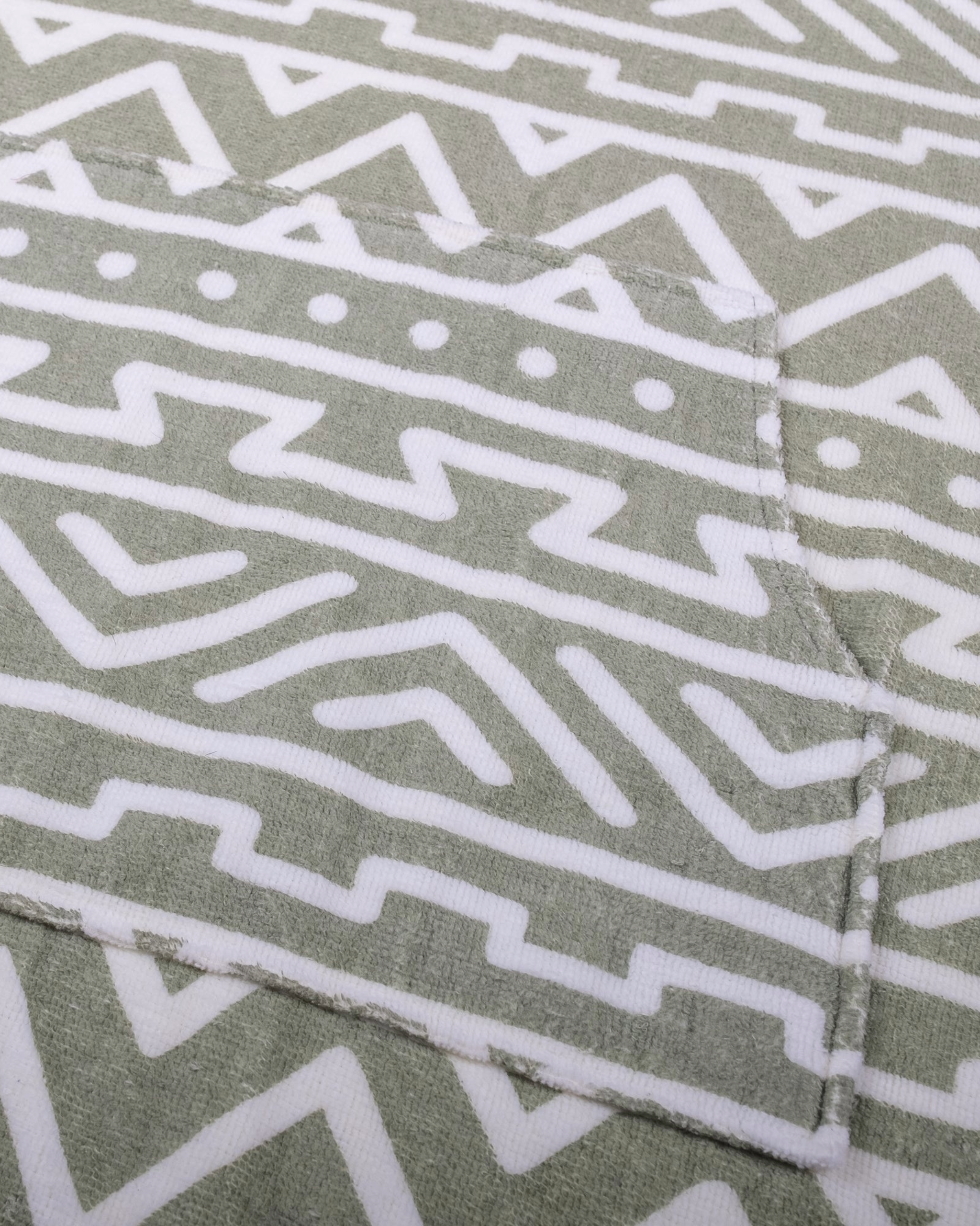 Close-up of beardedgoat’s Changing Towel shows a sewn pocket with white geometric tribal patterns on a muted green background. The pocket, outlined by stitching, blends seamlessly—making this towel a summer essential.