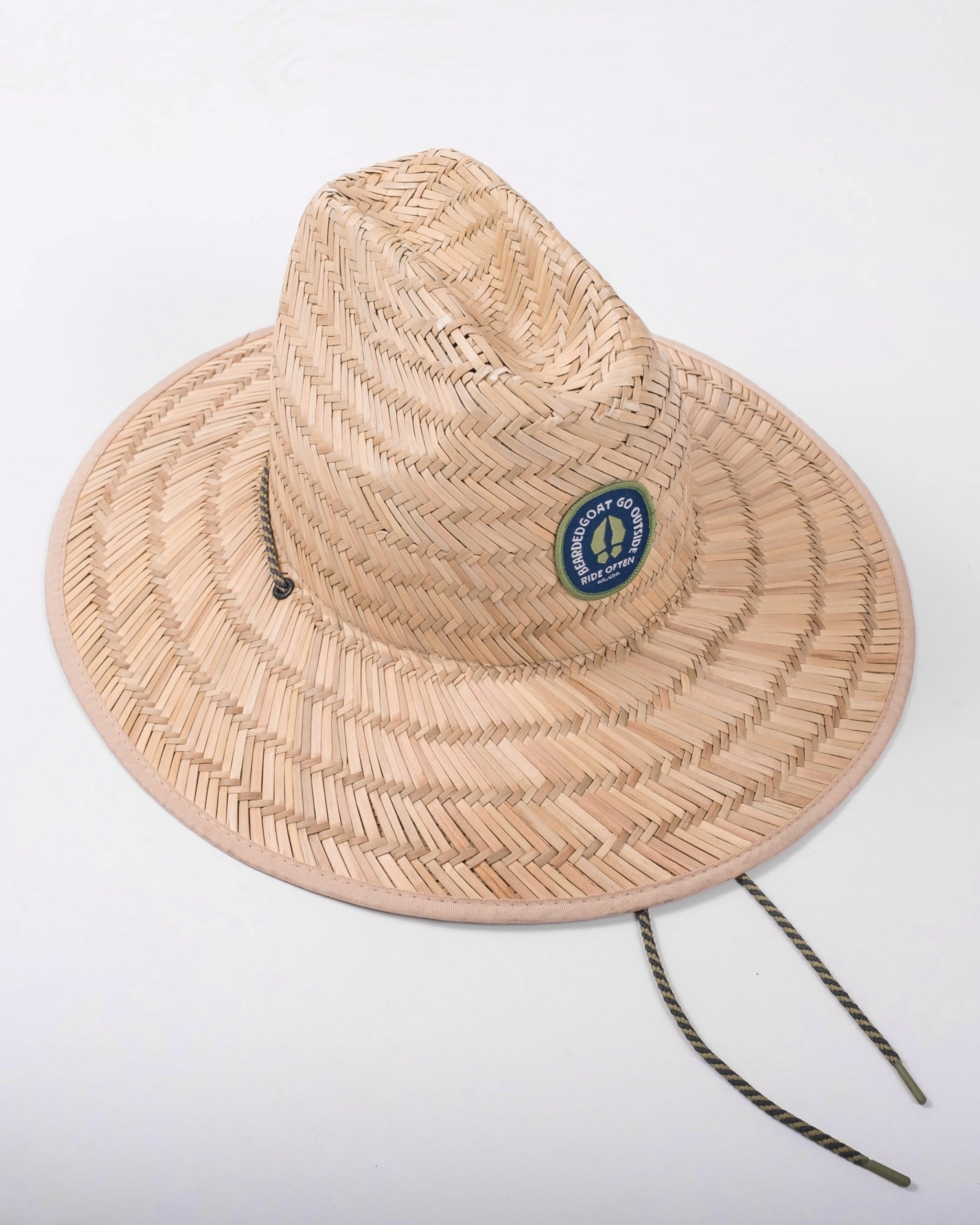 The beardedgoat Sun Hat features a wide straw brim, round GOAT 40th Anniversary patch, chin straps, and UV protection. It is displayed on a plain white background.