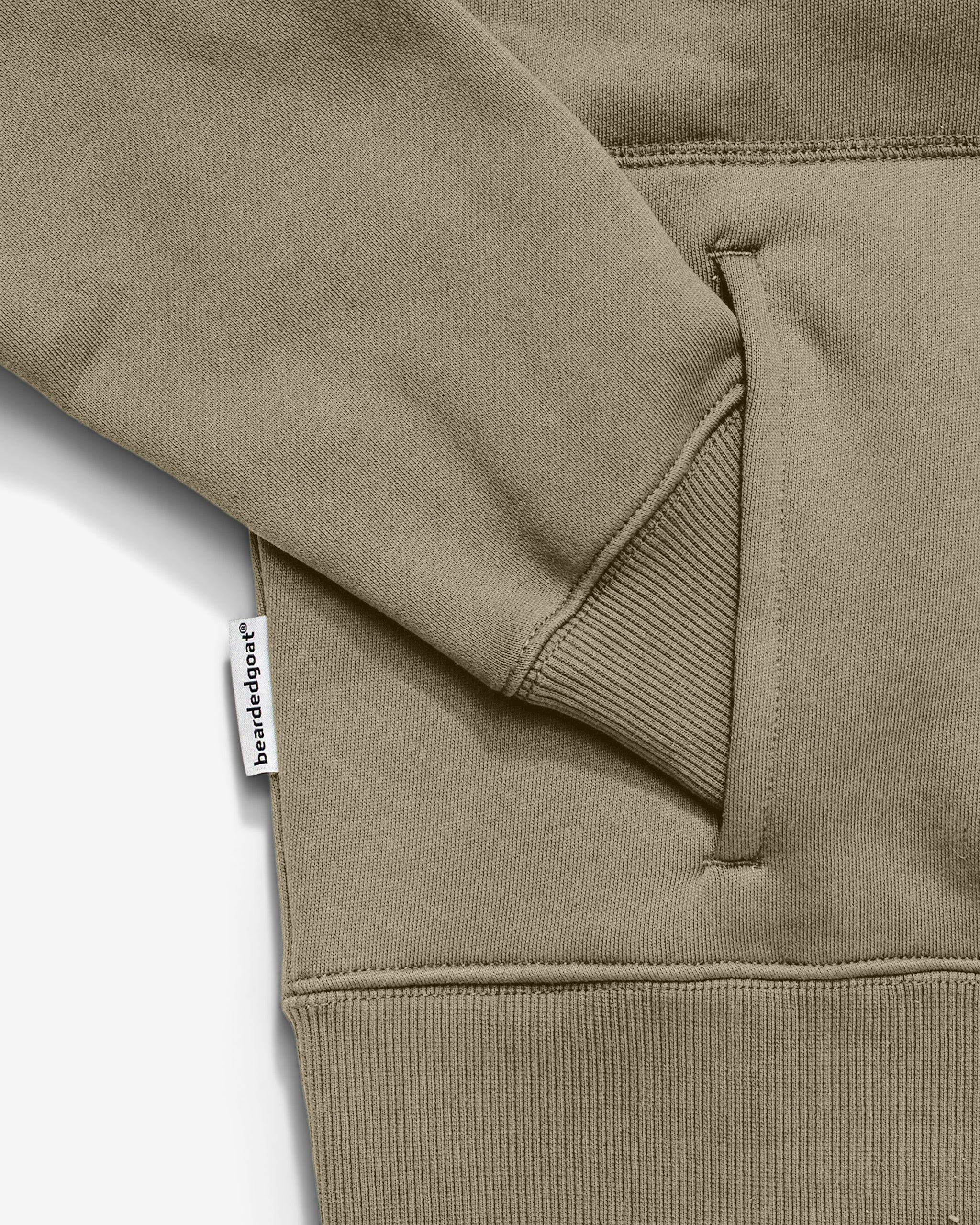 Close-up of the Women's Overnight™ Hoodie by beardedgoat in khaki, featuring ribbed cuffs, a visible white brandeddept tag by the pocket, and made from heavyweight cotton fleece for comfort.