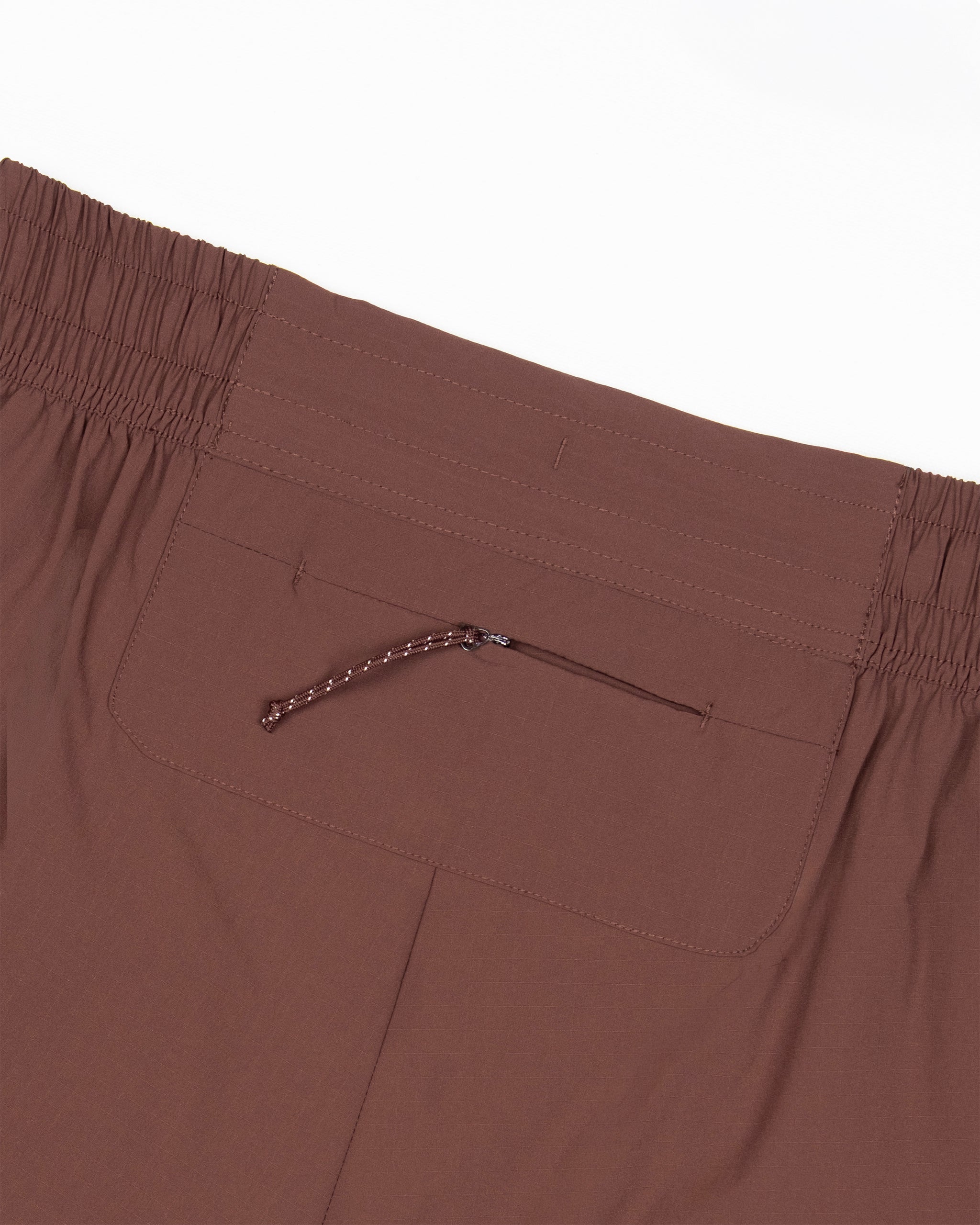 Close-up of the back of BEARDEDGOAT Women's Alpina Short in brown, showing durable ripstop fabric, a zippered pocket with cord pull, and visible stitching on the waistband and pocket.