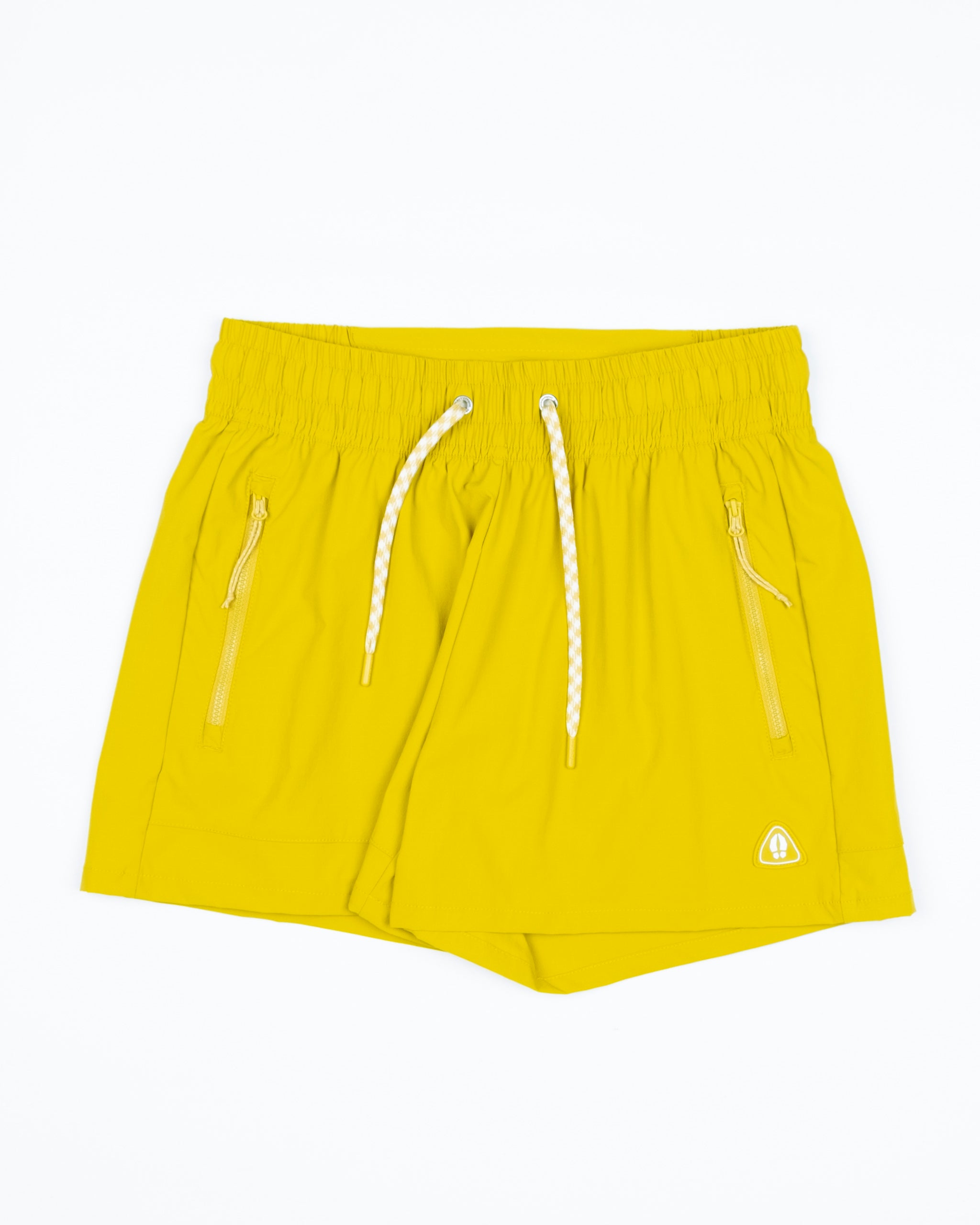 The BEARDEDGOAT Women's Alpina Short features bright yellow ripstop fabric, an elastic waistband with white drawstrings, two zippered pockets, and a small white logo on the front left leg. Shorts are shown laid flat on a white background.