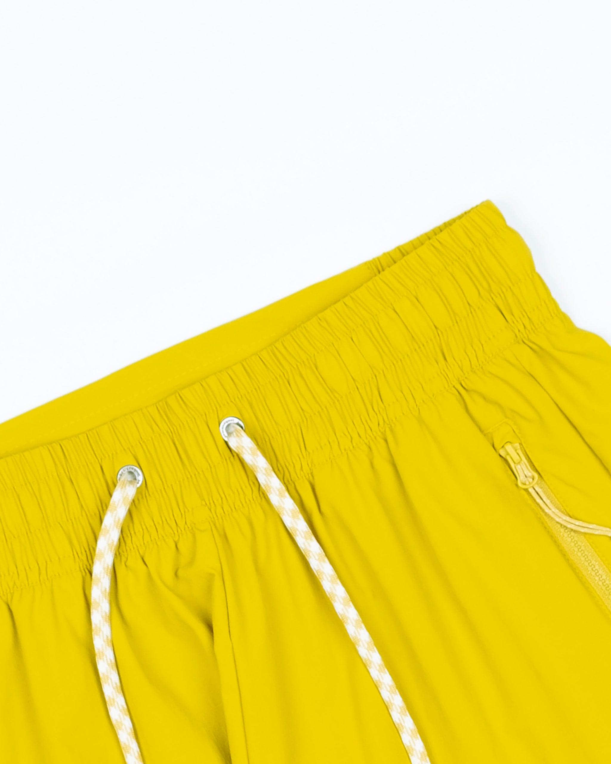 Close-up of the waistband of BEARDEDGOAT Women's Alpina Short in yellow ripstop, featuring a white drawstring and zippered pocket, shown against a white background.