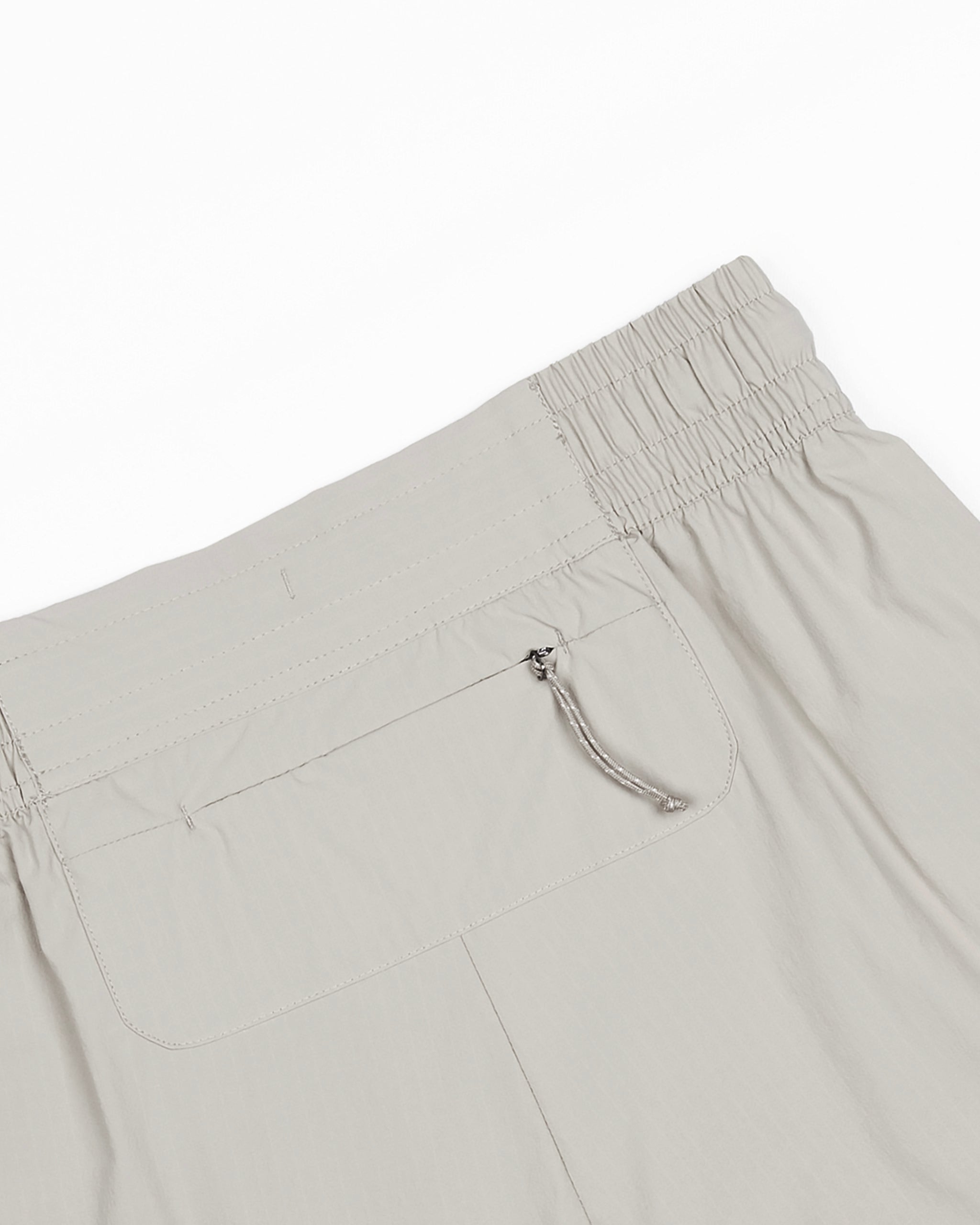 The BEARDEDGOAT Women's Alpina Short is shown from the back in light gray, featuring a right-side zippered pocket and a durable ripstop fabric with a multi-row elastic waistband for added stretch and comfort.