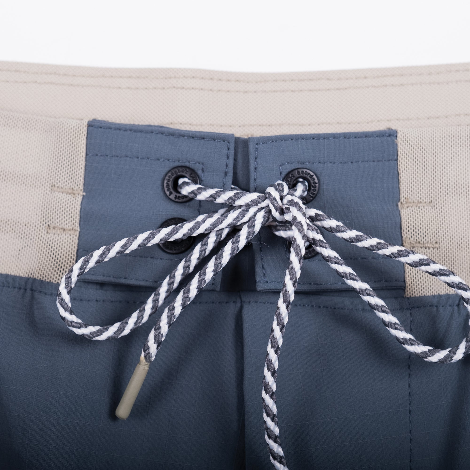 Close-up of the beardedgoat Mens Rambler Short waistband in blue, featuring a beige band and a black-and-white striped drawstring tied in a bow through metal grommets—made for trail running and extreme movement.